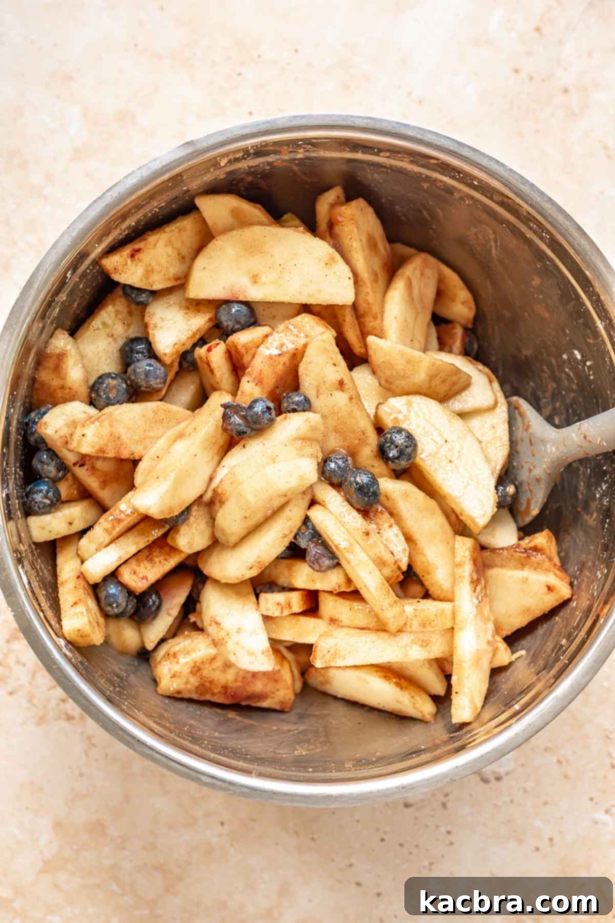 Sliced apples and blueberries mixed in a large bowl, coated with spices.