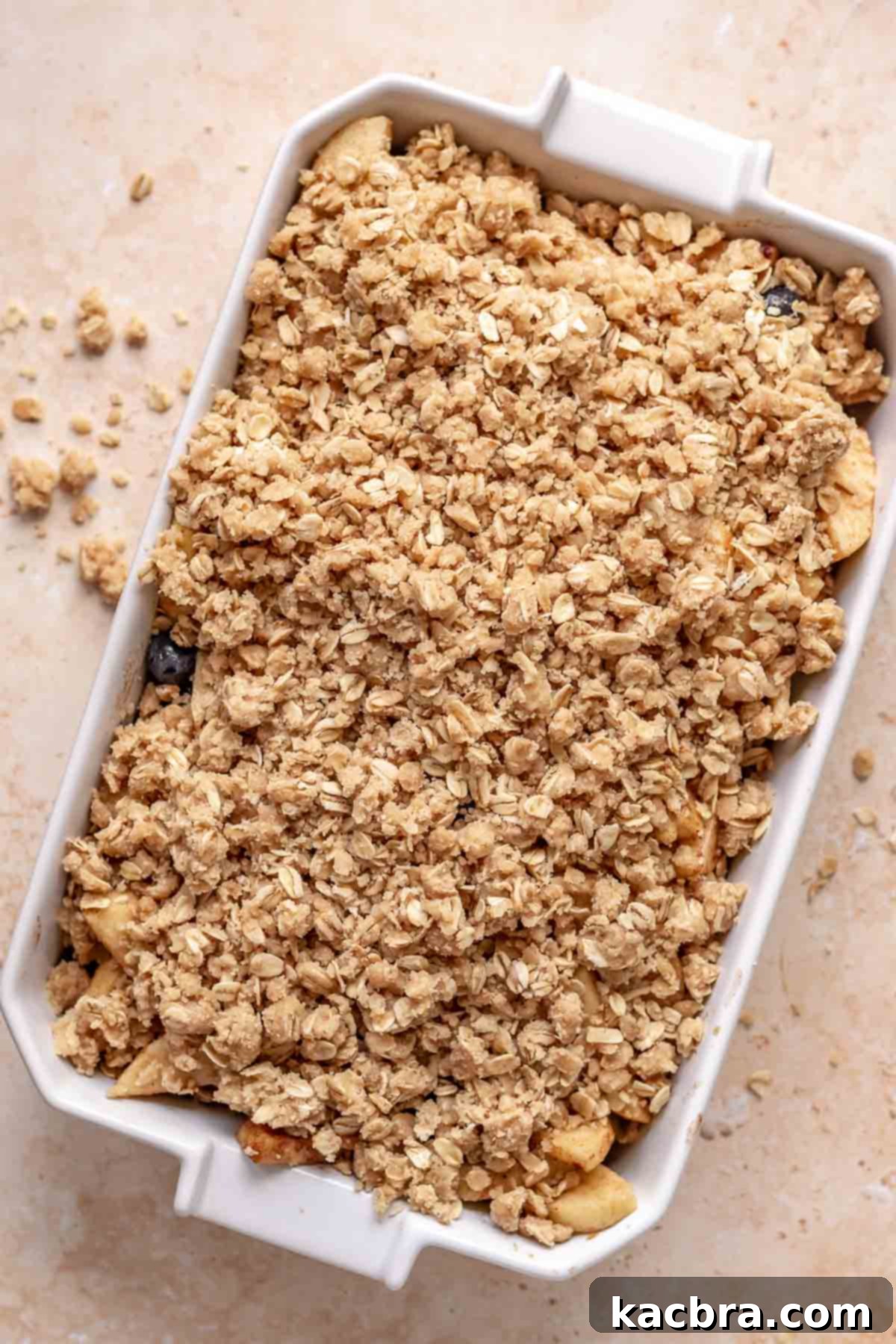Crisp topping scattered over apples and blueberries in a casserole dish before baking.