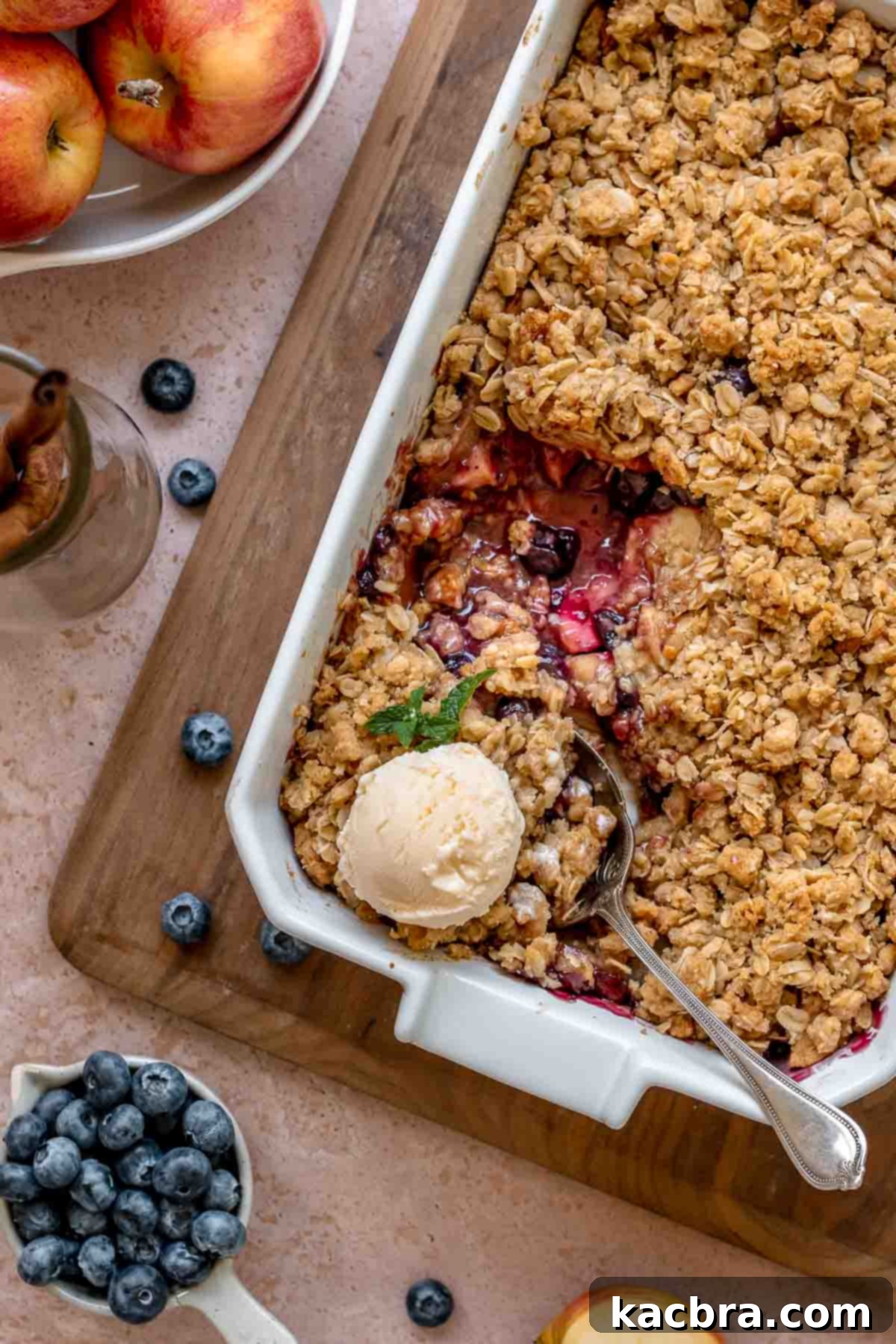 Finished apple blueberry crisp in a casserole dish with a scoop removed and vanilla ice cream melting on top.
