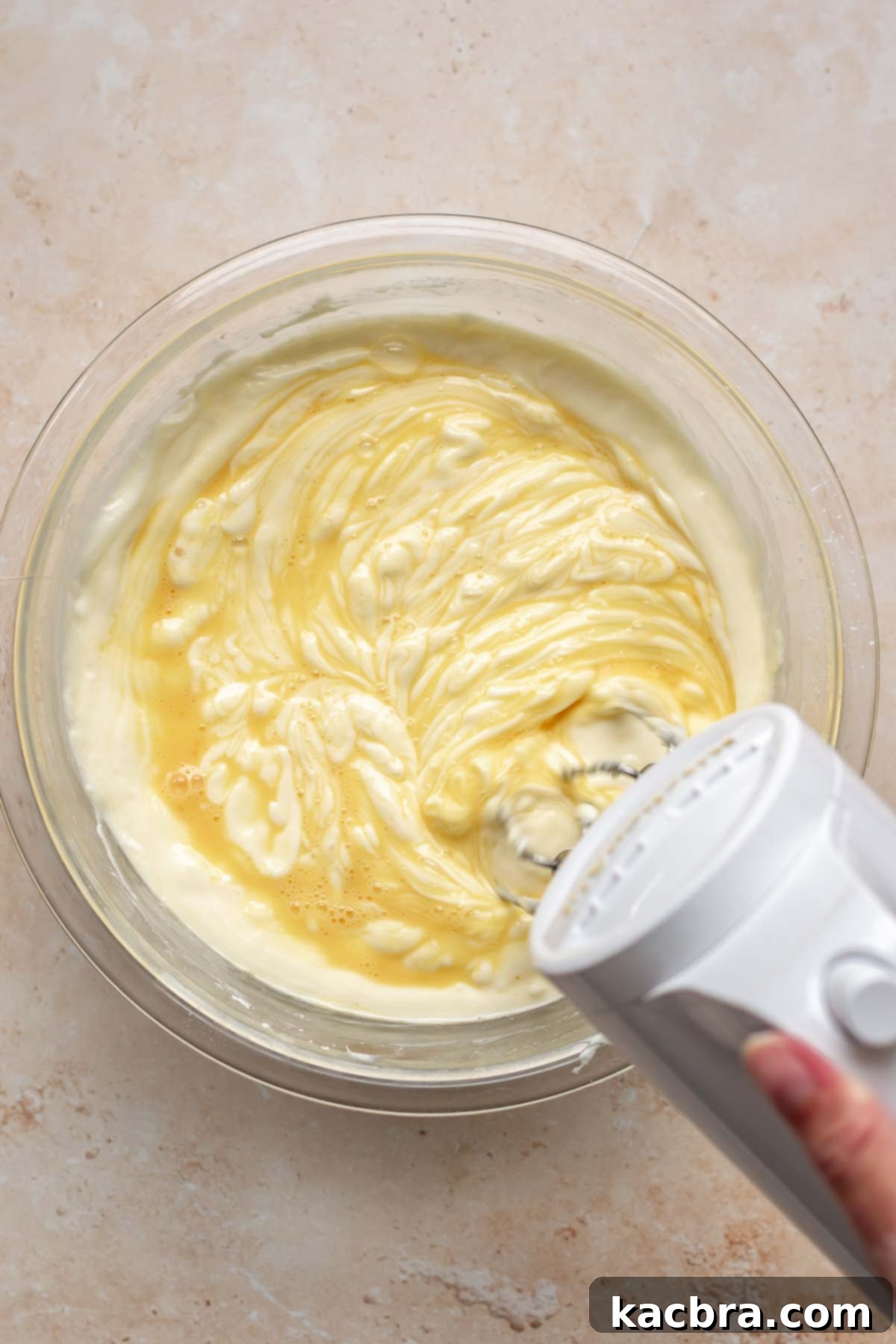 A mixer beats whisked eggs into cheesecake batter.