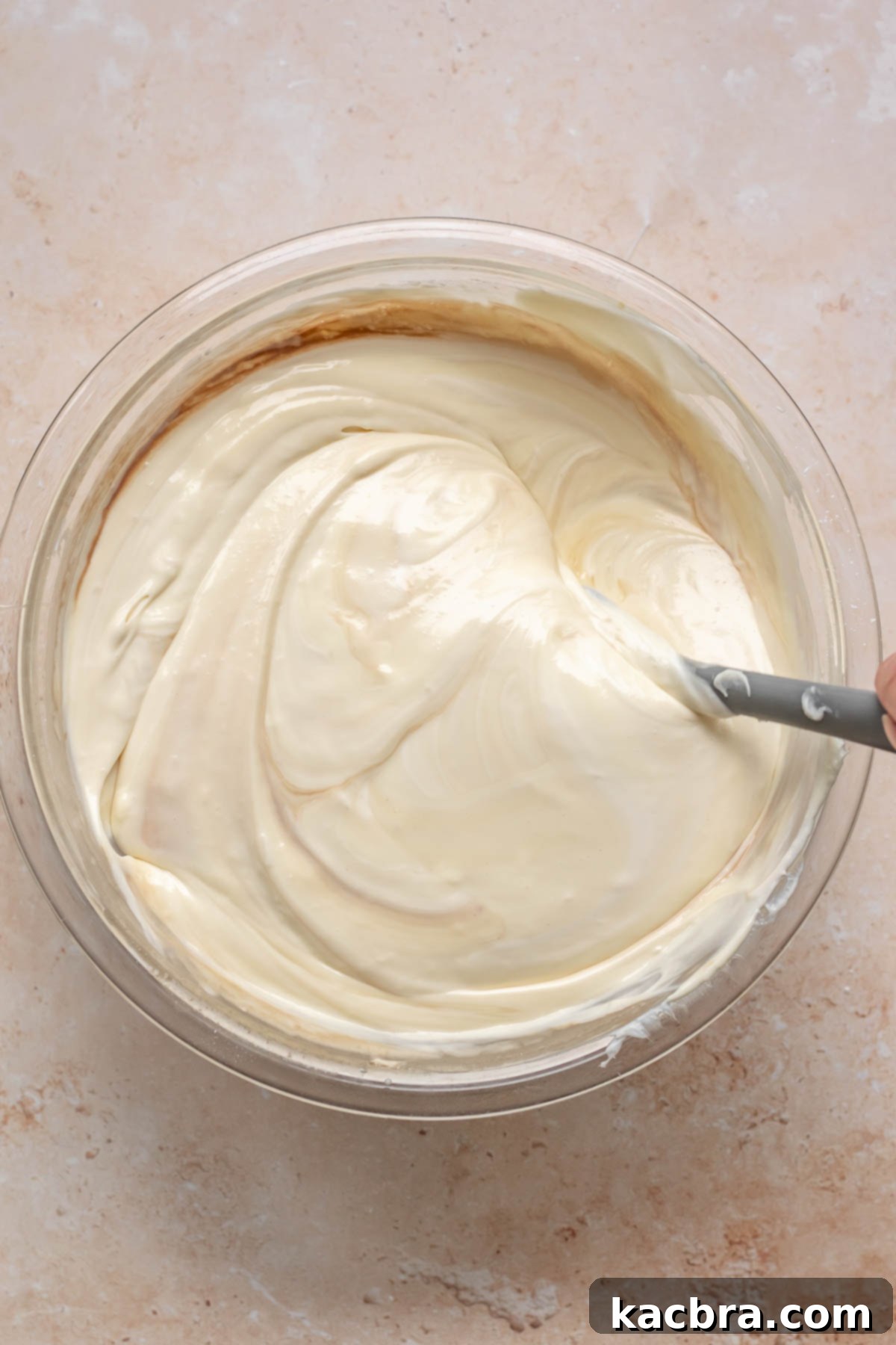 A spatula folds sour cream and vanilla into cheesecake batter.