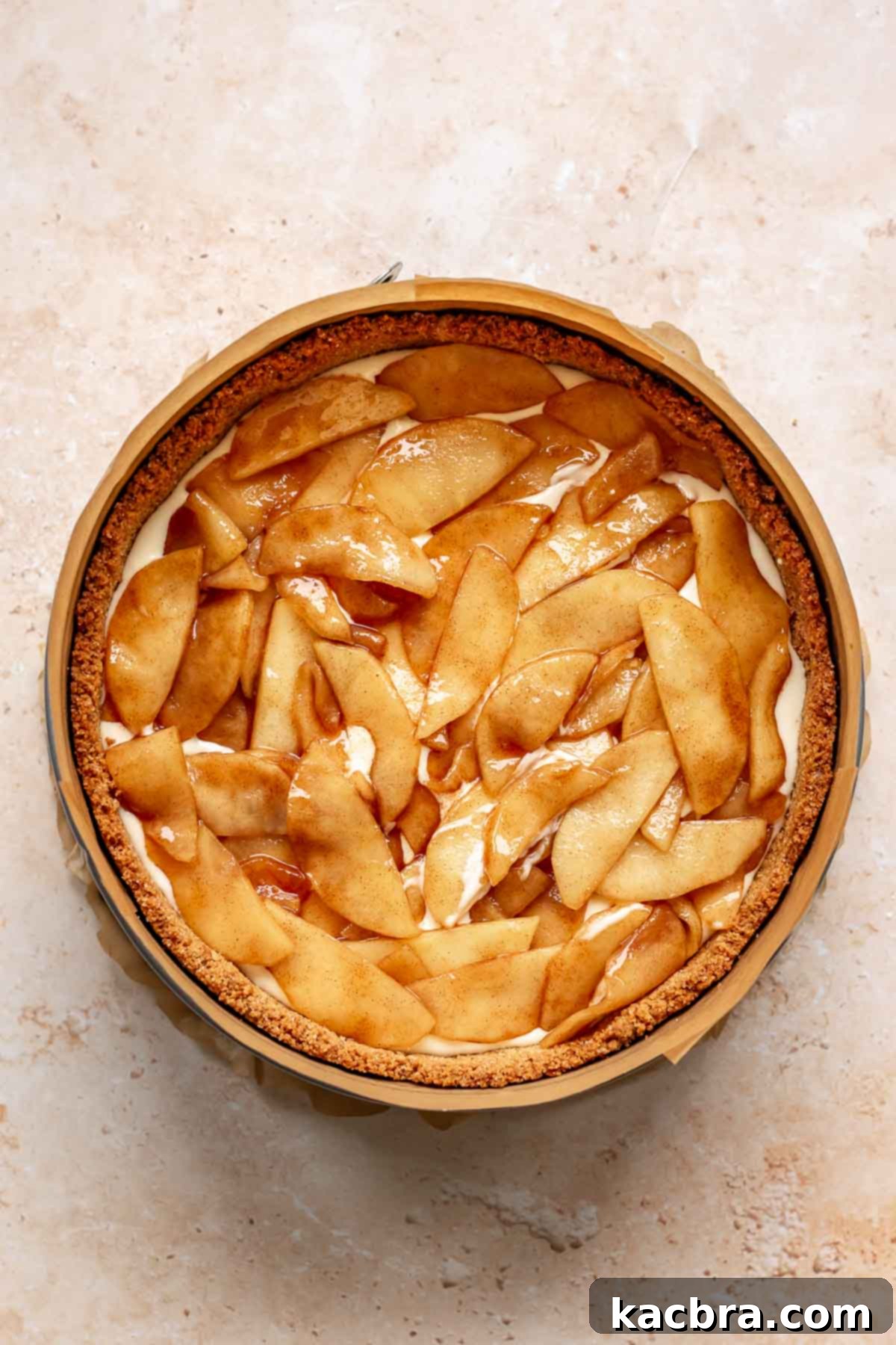 Apple pie filling on top of cheesecake batter in a pan.