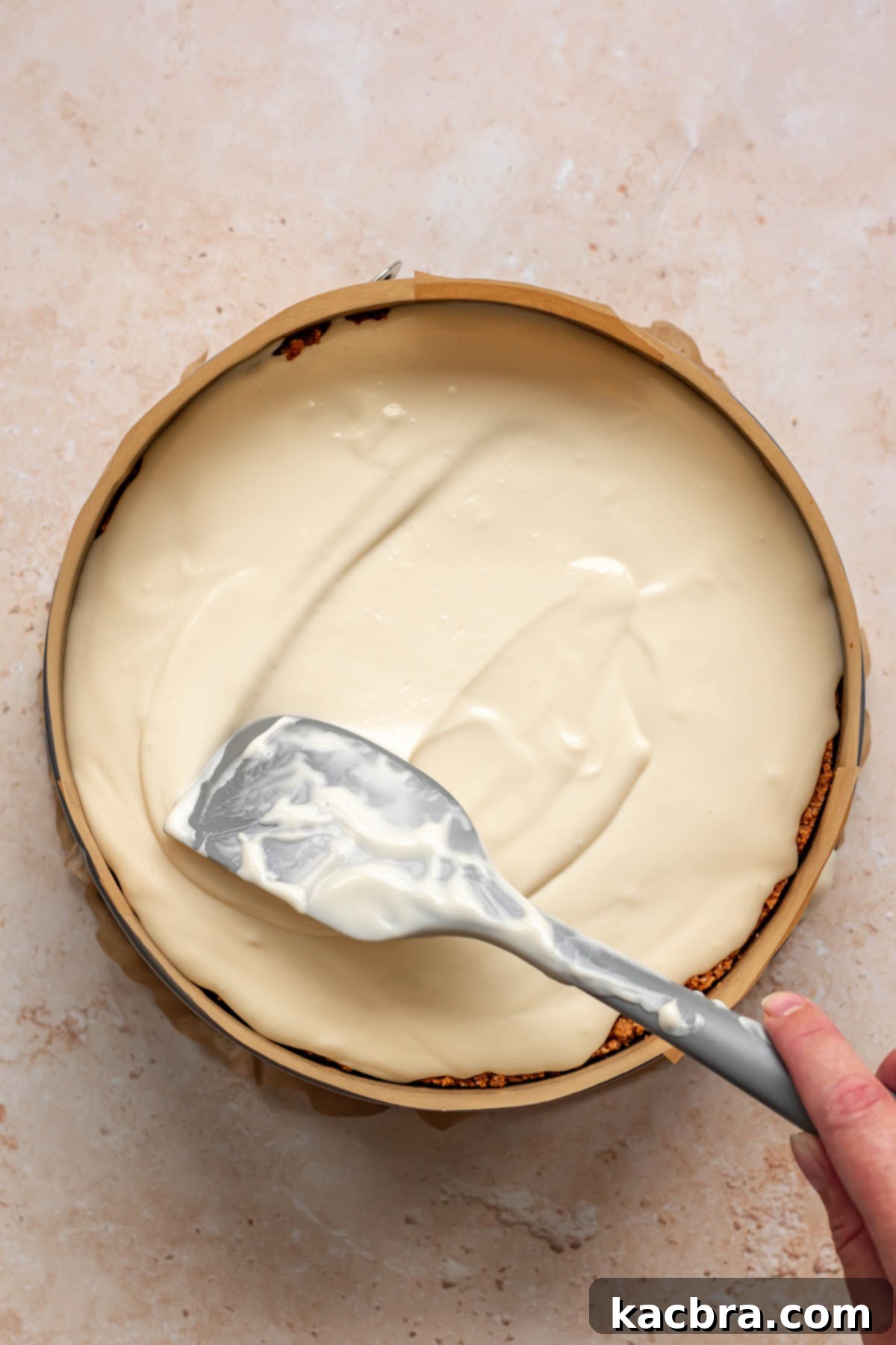 A spatula spreads cheesecake batter evenly.