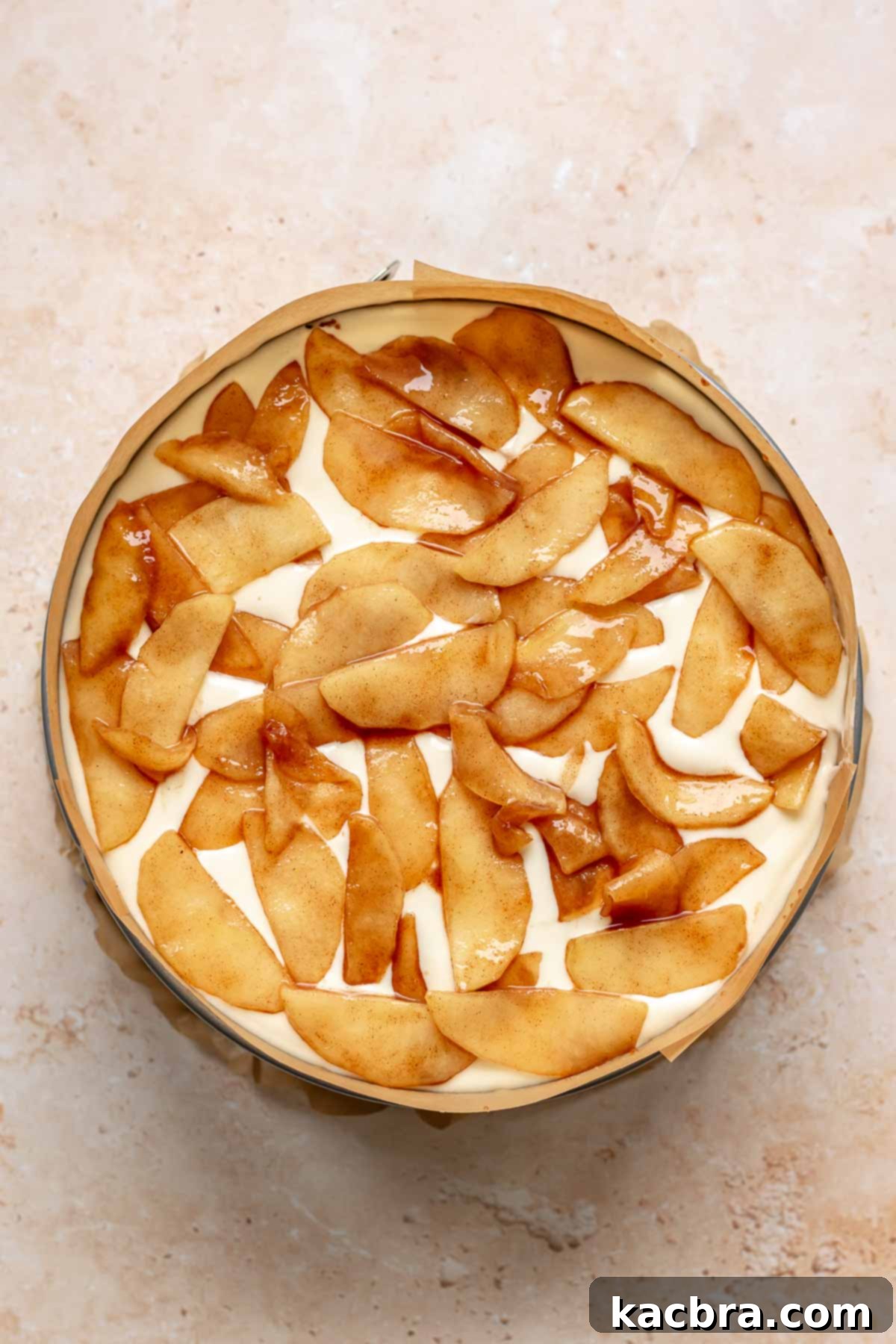 Apple pie filling on top of cheesecake batter in a pan.