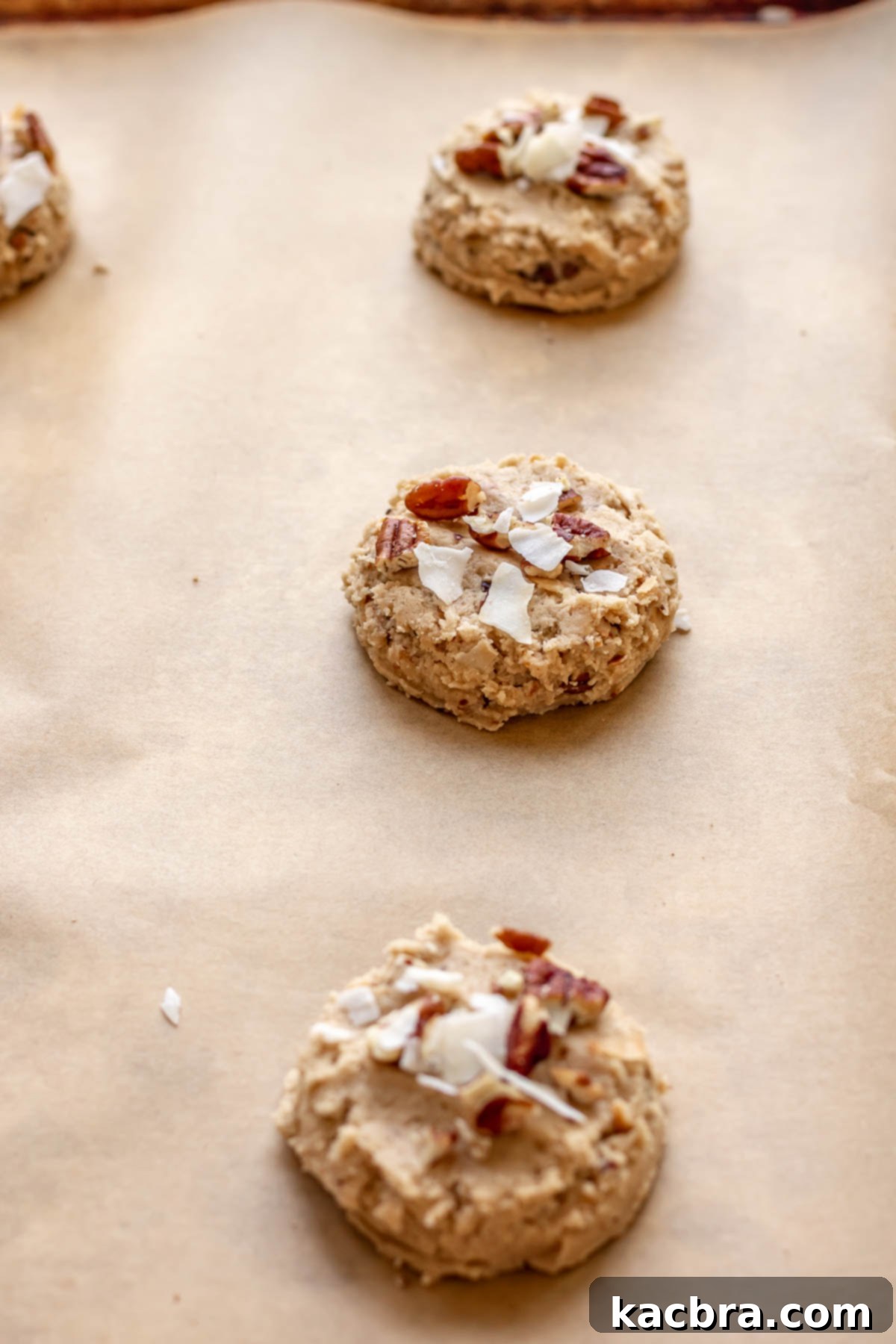 Cookie dough balls adorned with extra untoasted coconut flakes and pecans on a baking sheet, ready for the oven.