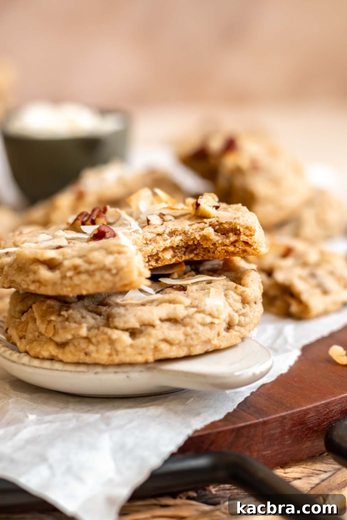 Two perfectly stacked coconut pecan cookies on a small white plate, with a bite taken out of the top cookie to show its texture.