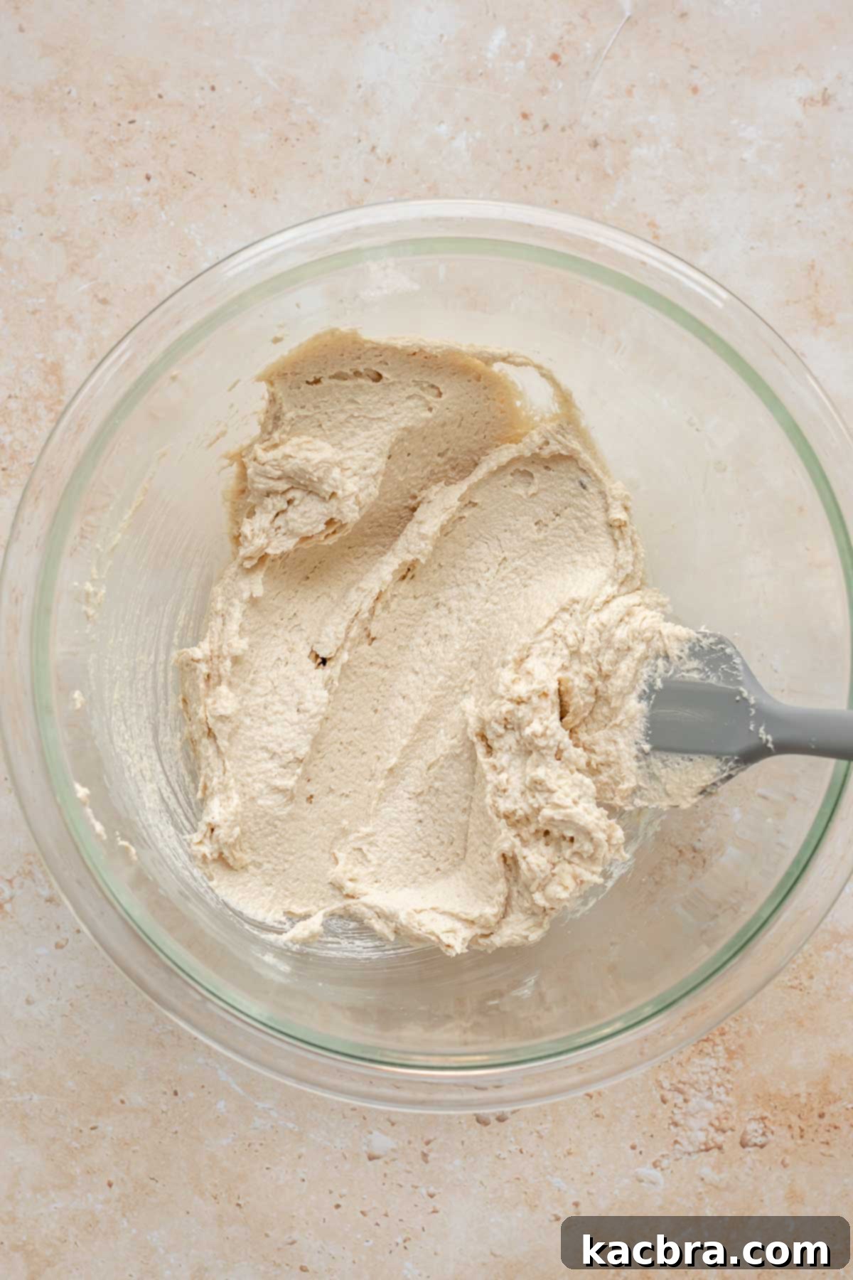 Creamed unsalted butter and sugars in a mixing bowl with a rubber spatula, showing a light and fluffy texture.
