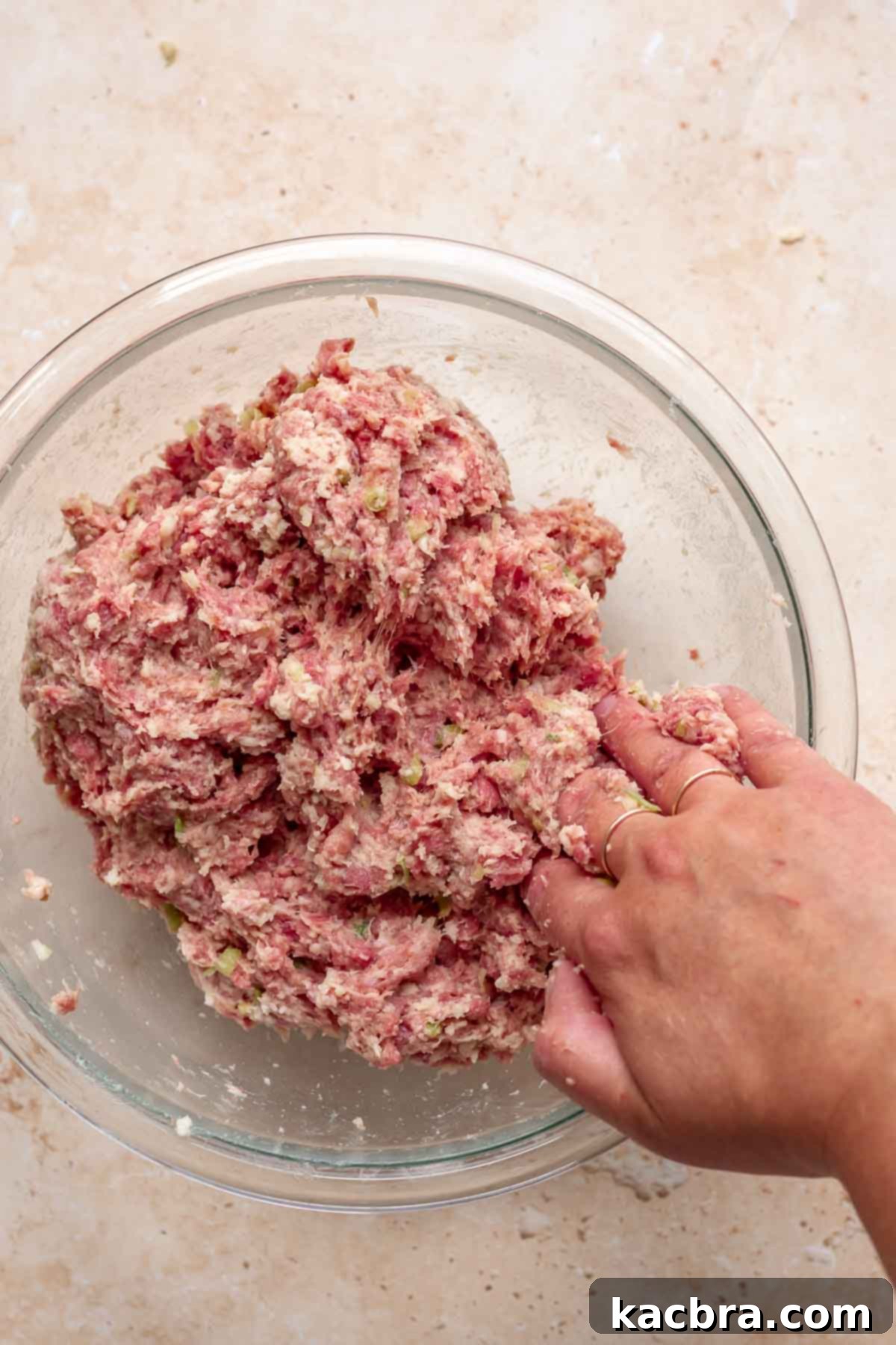 A hand mixes soaked breadcrumbs into meatball mixture.