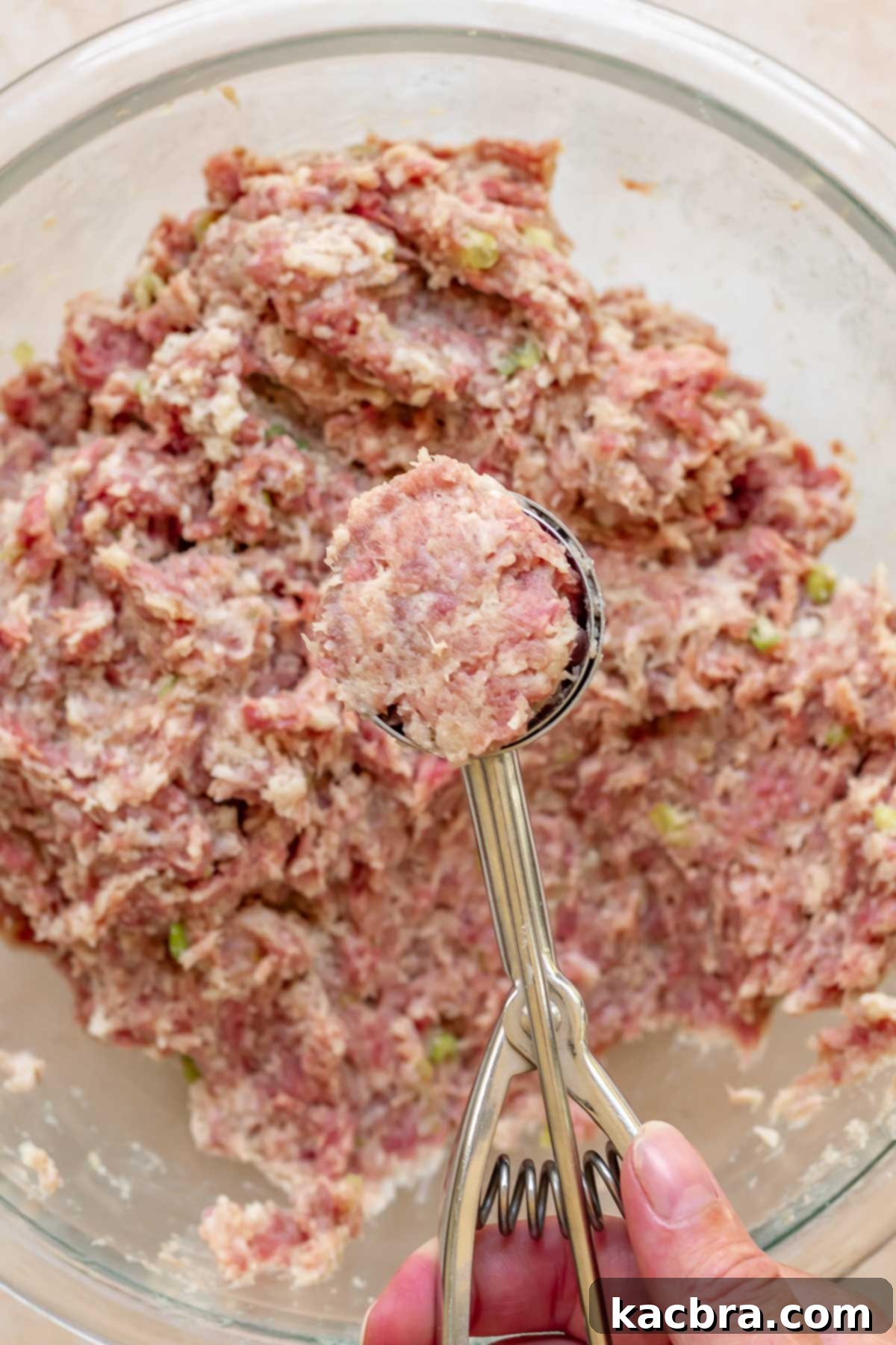 A cookie scoop holds a flush scoop of raw meatball meat.