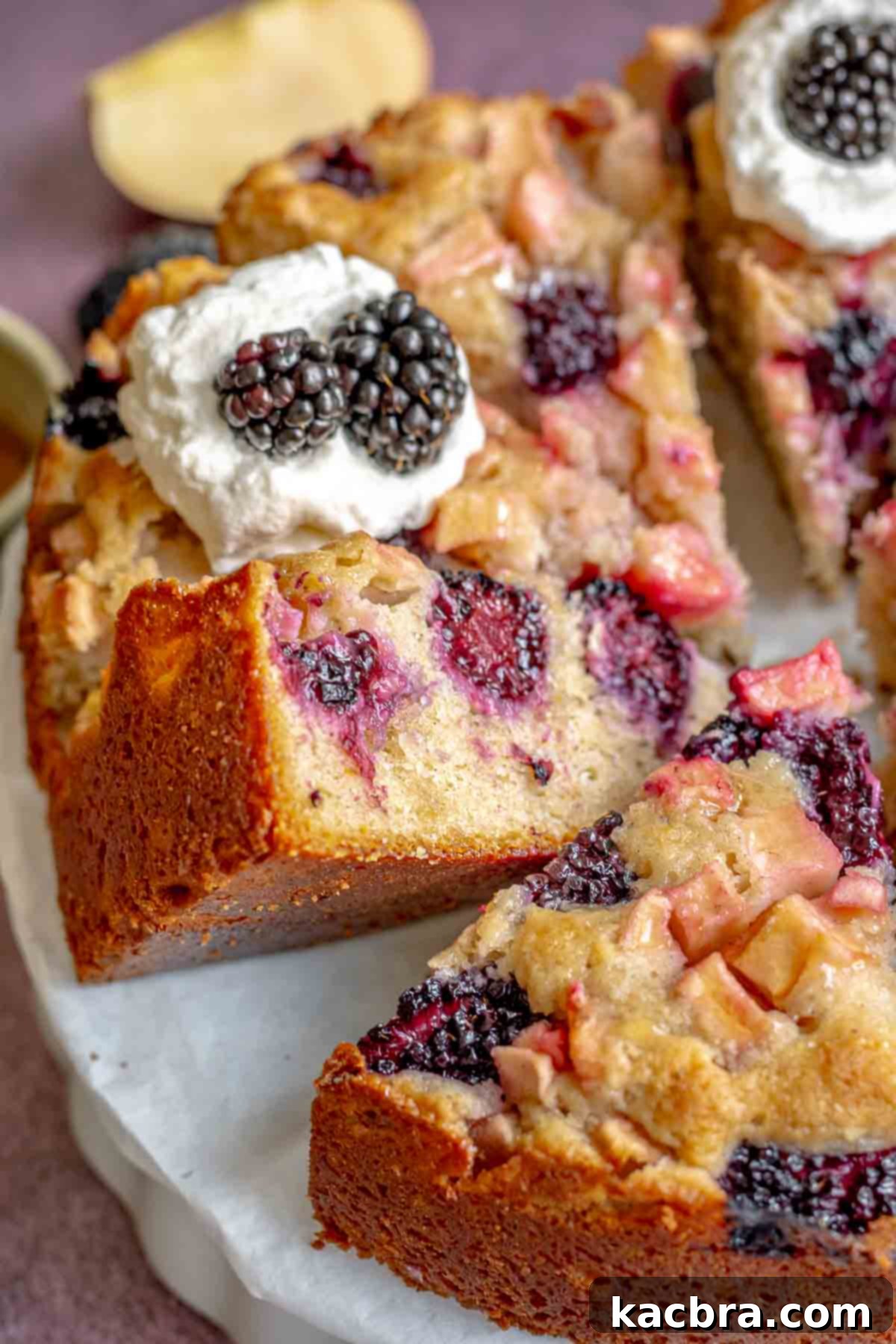 A platter of sliced apple blackberry cake with one piece leaning, showcasing the fluffy texture.