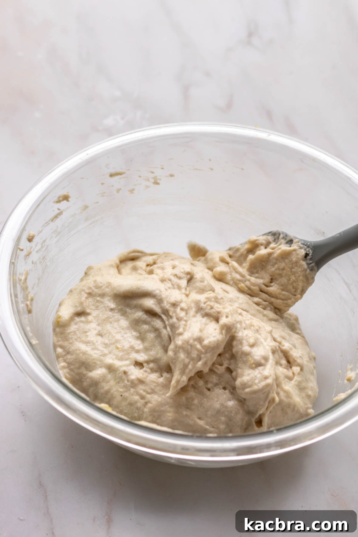 A rubber spatula folding the remaining flour into the cake batter by hand.