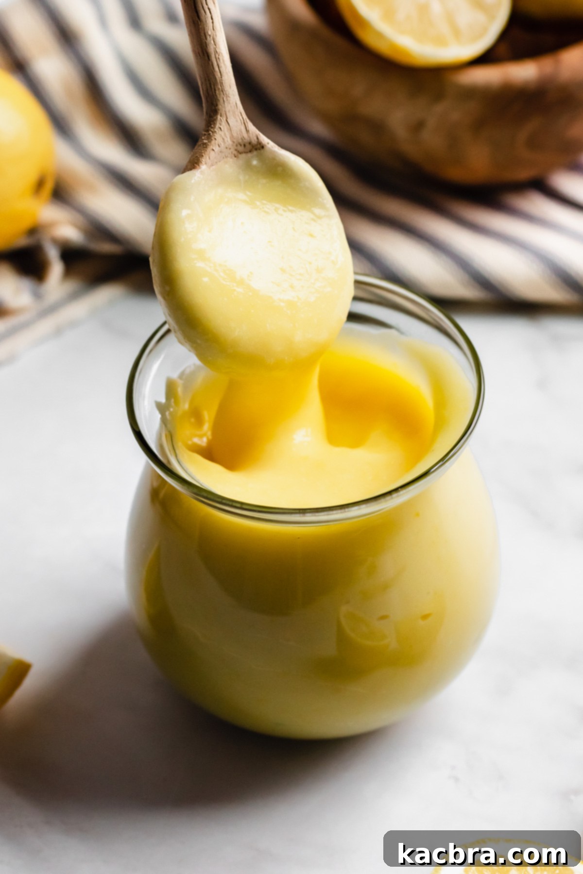 Thick and luscious lemon curd being pulled up with a spoon from a glass jar, showcasing its rich, golden texture.
