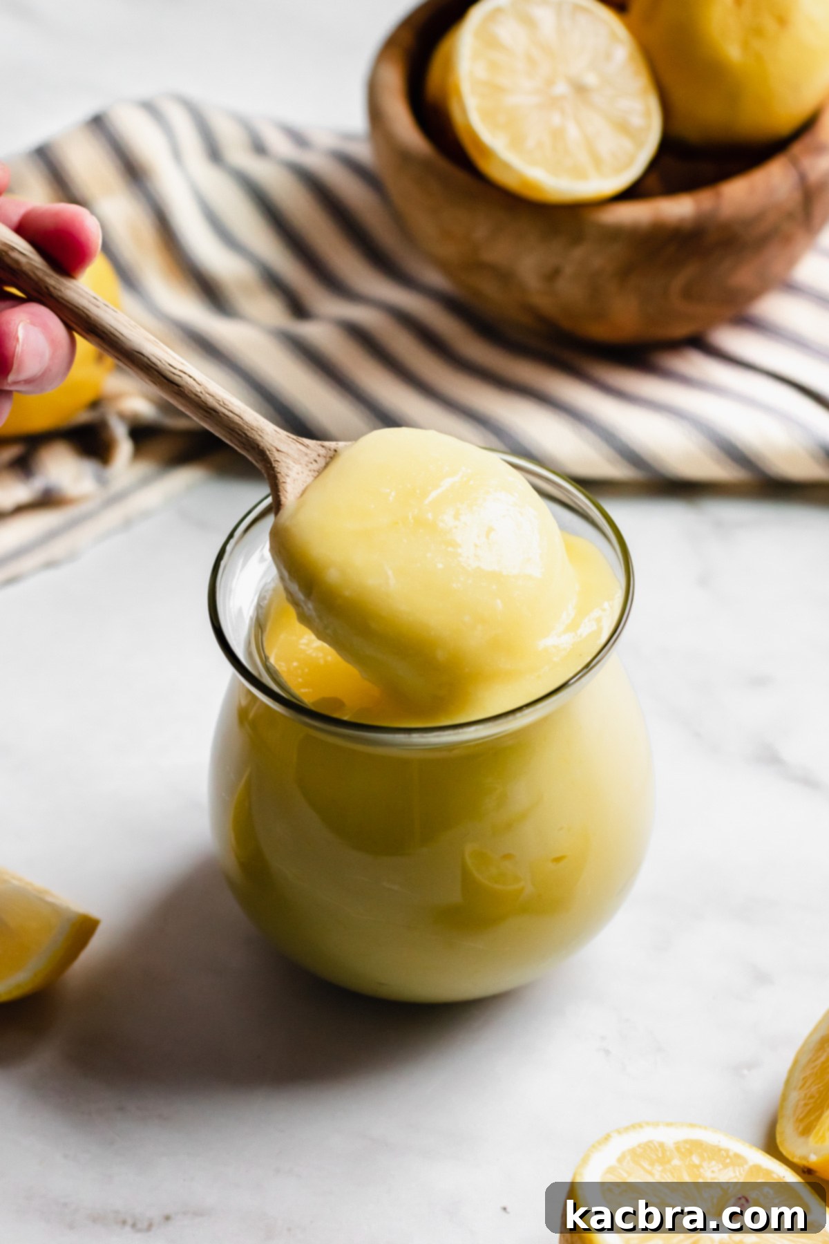 A close-up shot of a spoon expertly pulling thick, creamy lemon curd out of a glass jar, perfectly showcasing its ideal consistency and luxurious texture.