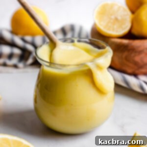 A glass jar filled with luscious lemon curd, with some gracefully spilling over the side, emphasizing its rich, vibrant yellow color and smooth texture.