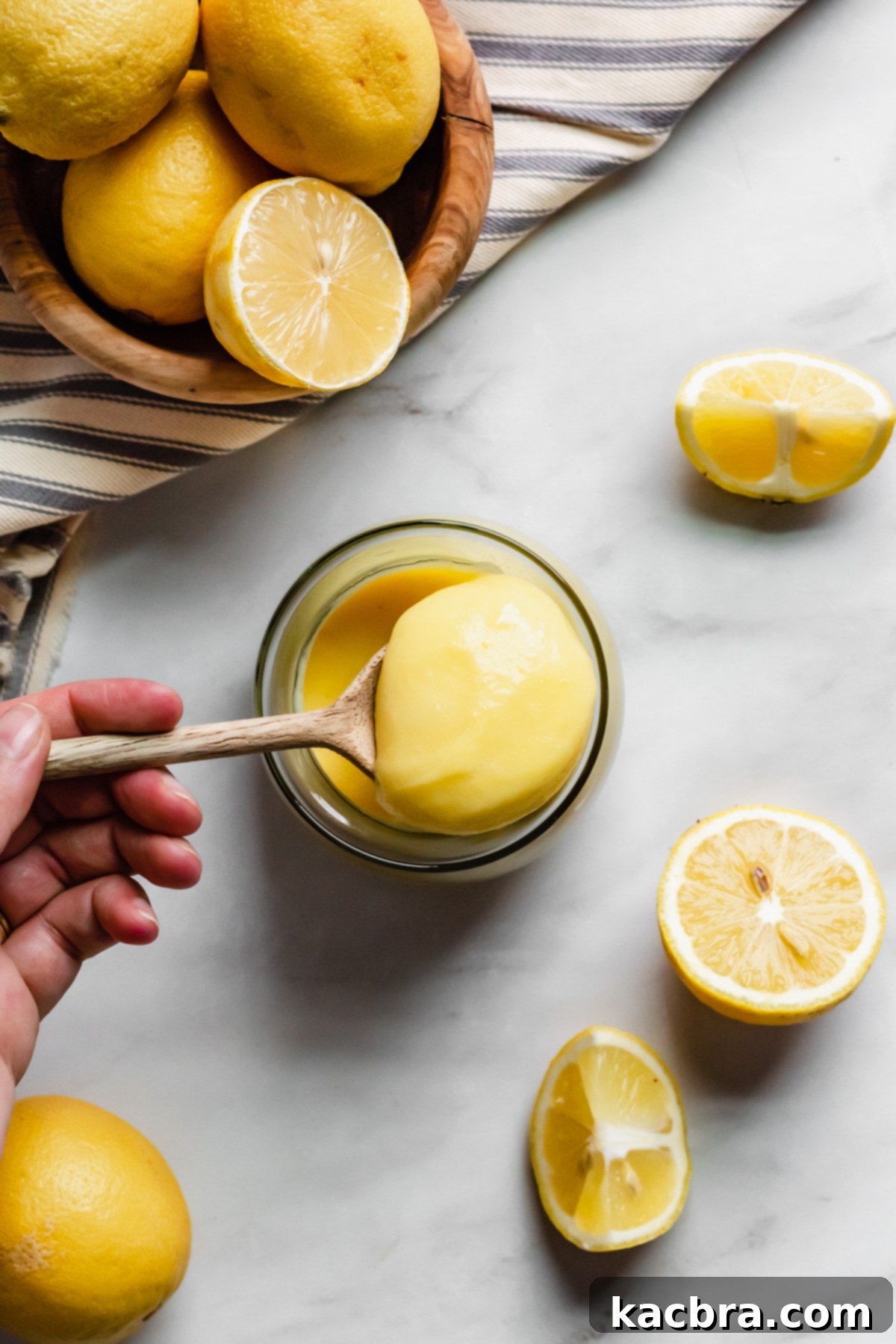 An inviting overhead shot of rich, creamy lemon curd presented in a elegant glass jar, accompanied by a spoon, highlighting its impeccable, smooth texture.