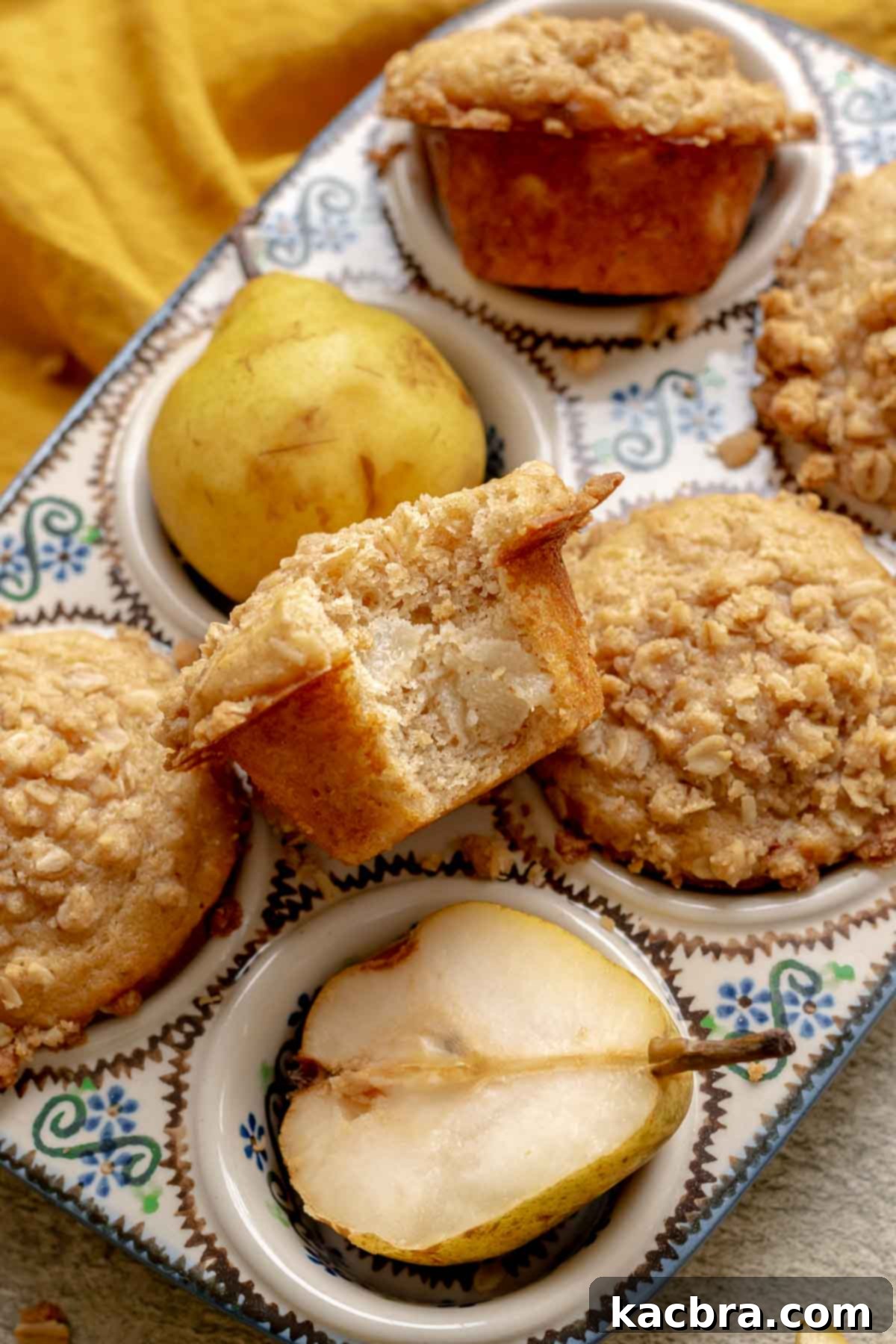 Baked pear muffins in a muffin tin. One sits in the middle with a bite removed, revealing the soft interior and pear pieces.
