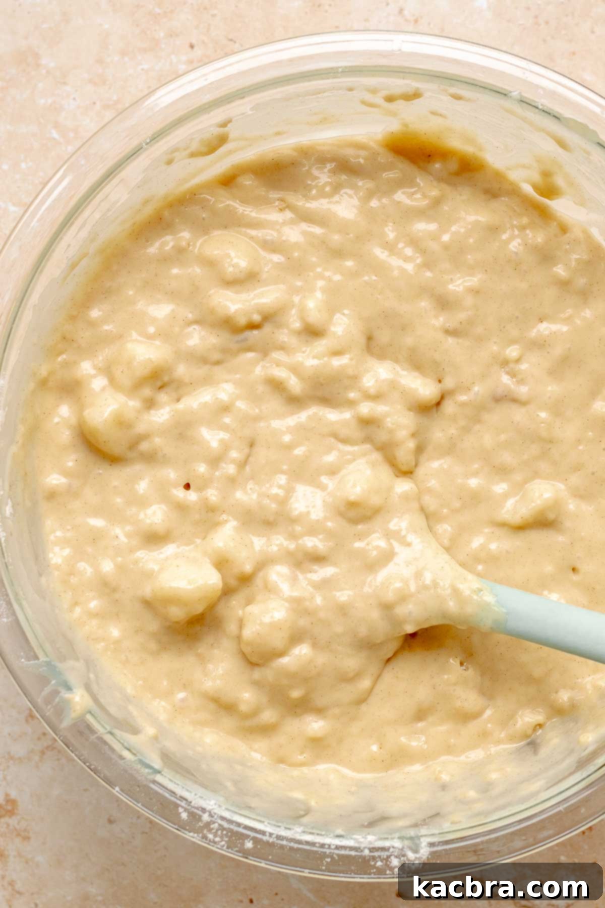 A rubber spatula gently folds pear chunks into muffin batter.