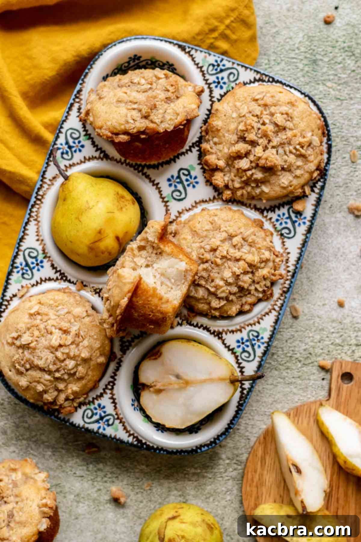 Baked pear muffins cooling in a muffin tin, with one muffin having a bite removed.