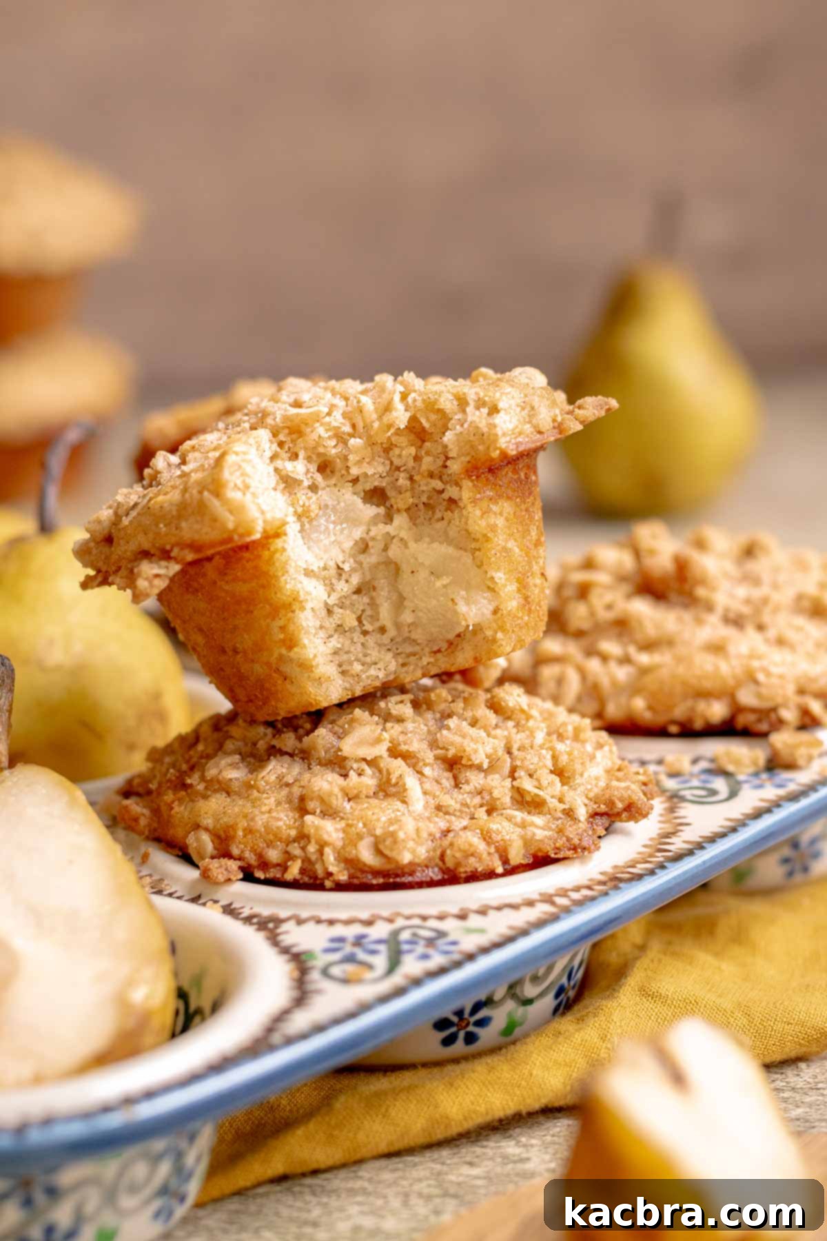 Two pear muffins stacked on top of each other, in a muffin tin, showcasing their golden streusel tops.