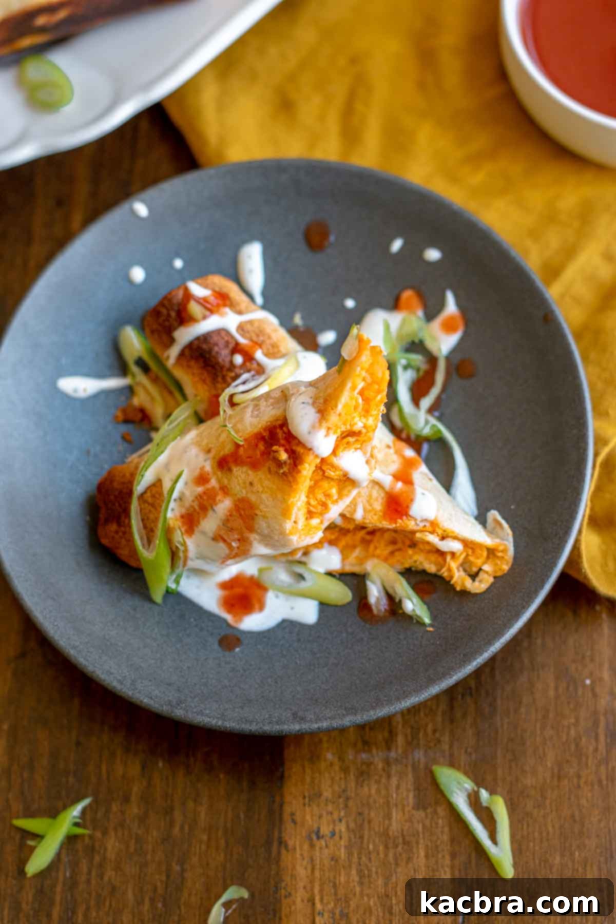 A perfectly cooked buffalo chicken taquito, cut in half to show the filling, garnished with ranch and buffalo sauce.