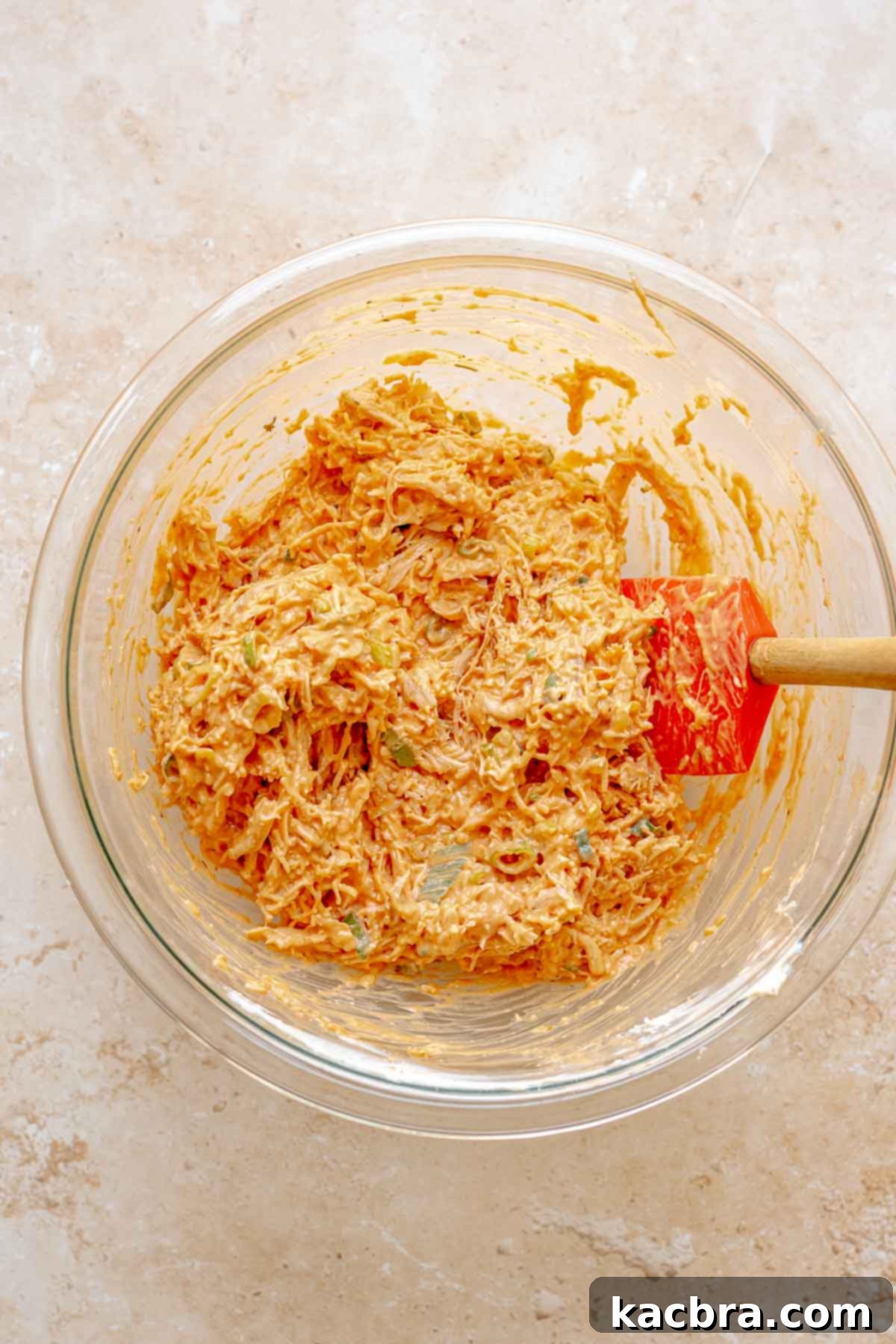 Shredded chicken being folded into the buffalo cheese mixture in a bowl.