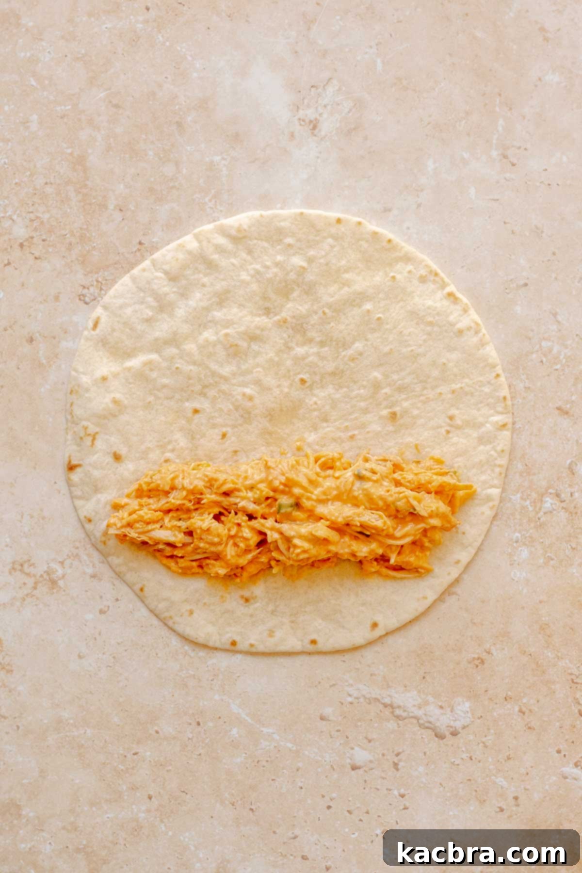 A line of buffalo chicken dip filling placed on the bottom third of a flour tortilla.
