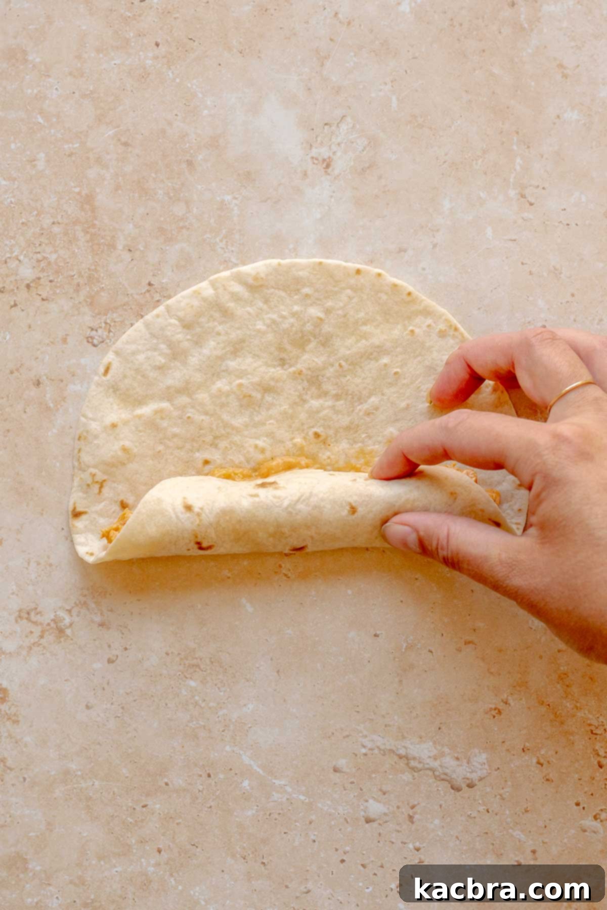 A hand demonstrating how to roll a tortilla with buffalo chicken filling.