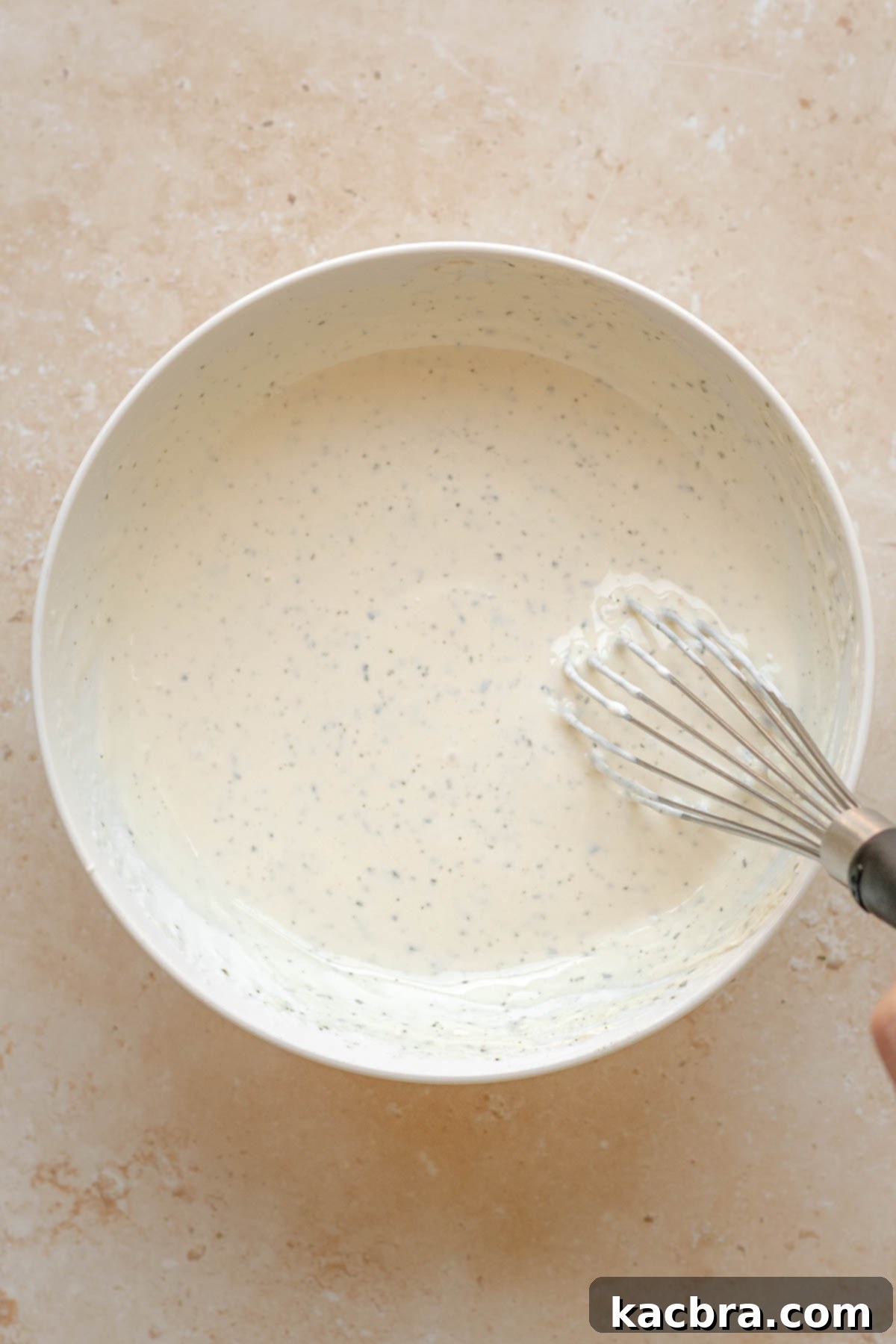 A whisk mixing homemade ranch dip ingredients in a bowl.