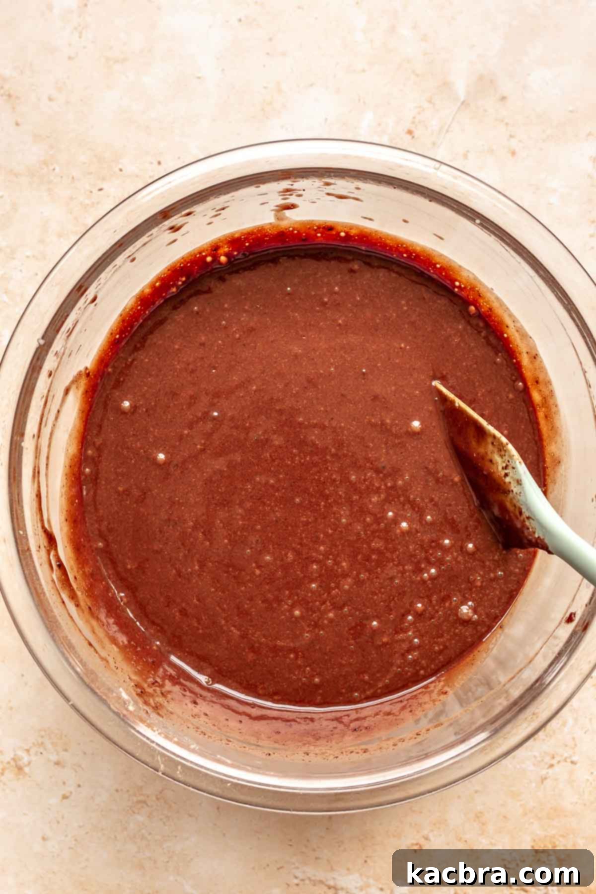 Decadent Chocolate Walnut Dream 9 Thin chocolate cake batter being stirred gently with a rubber spatula, showing its liquid consistency after all ingredients have been incorporated.