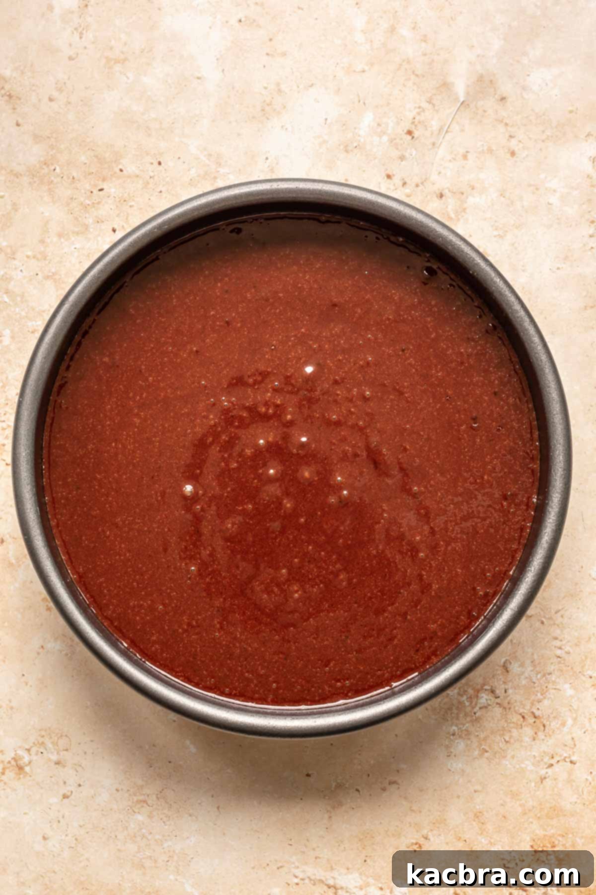 Chocolate cake batter in a cake pan before baking.