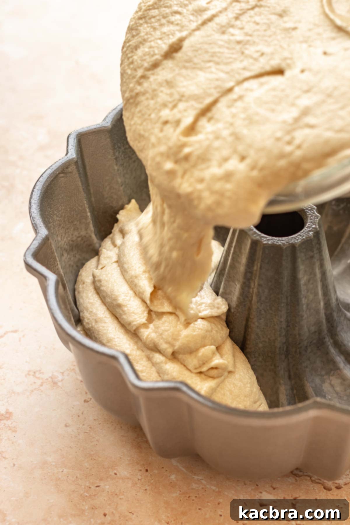 Cake batter being poured into a prepared bundt pan.