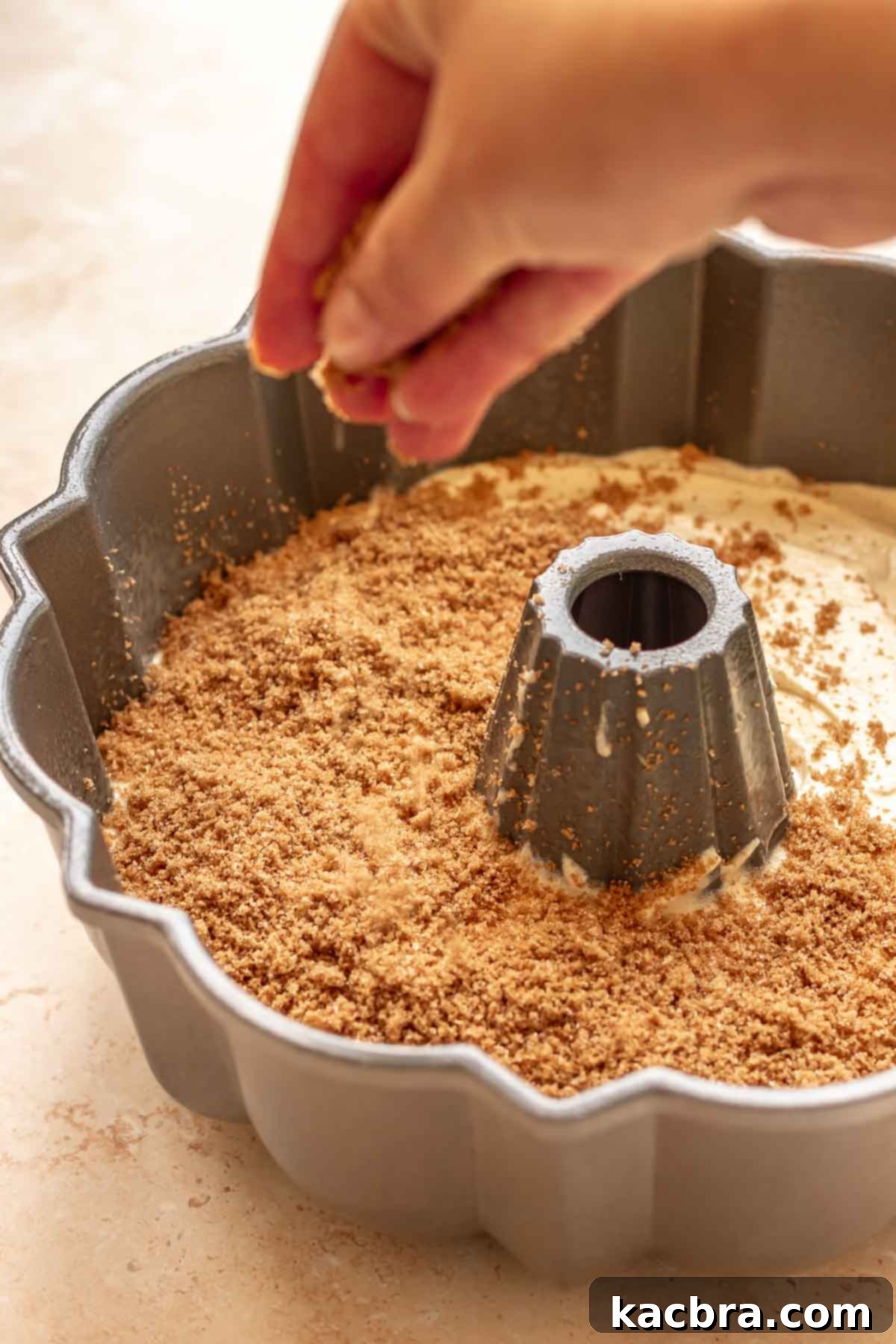 A hand adds cinnamon sugar to the top of the cake batter.