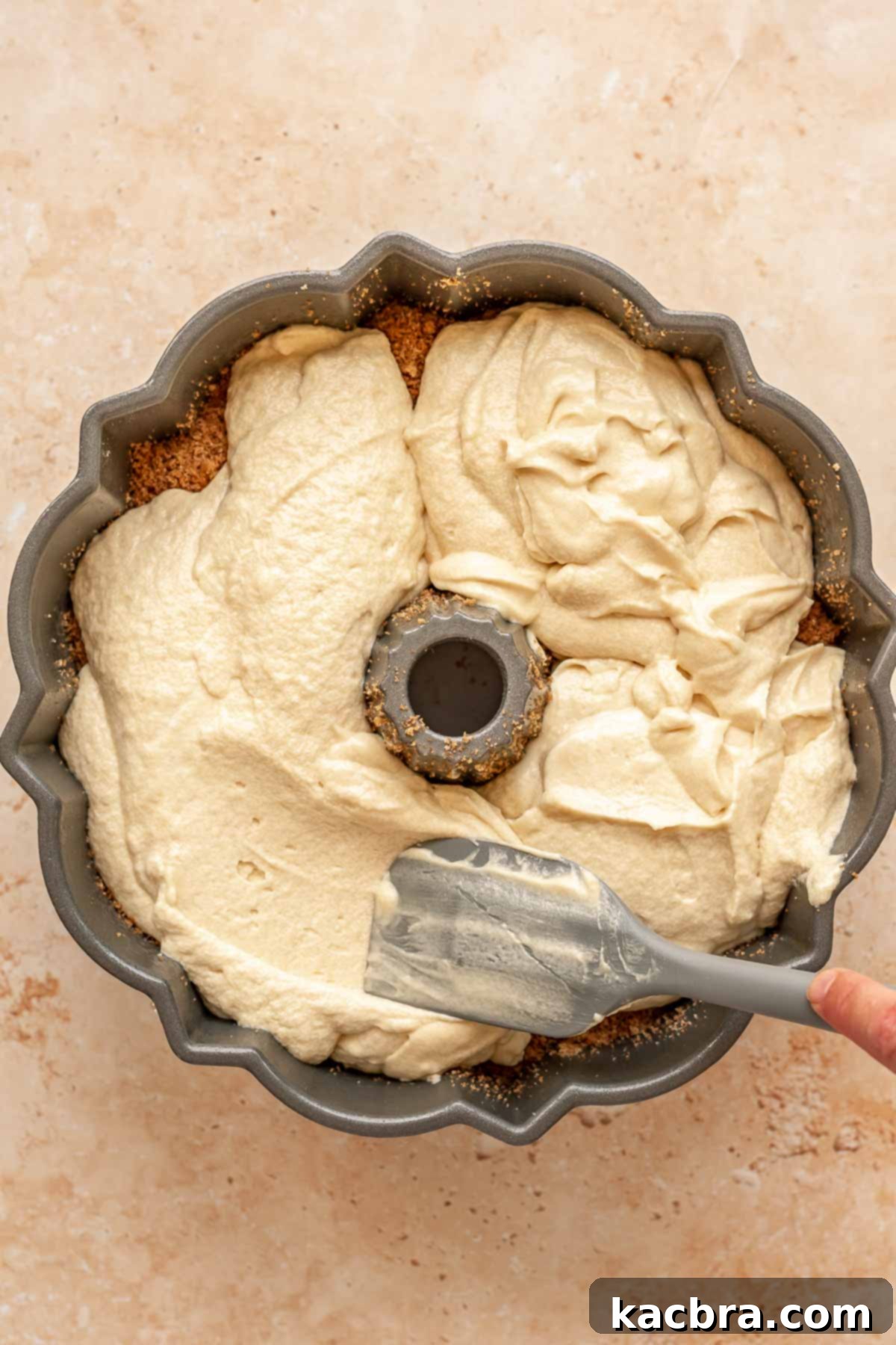 A spatula spreads cake batter on top of the cinnamon sugar.