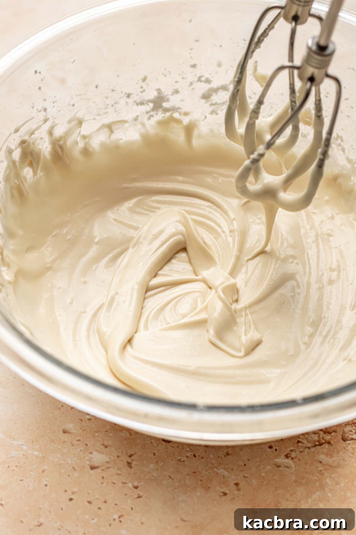 Hand mixer beaters drip cream cheese frosting off into a bowl.