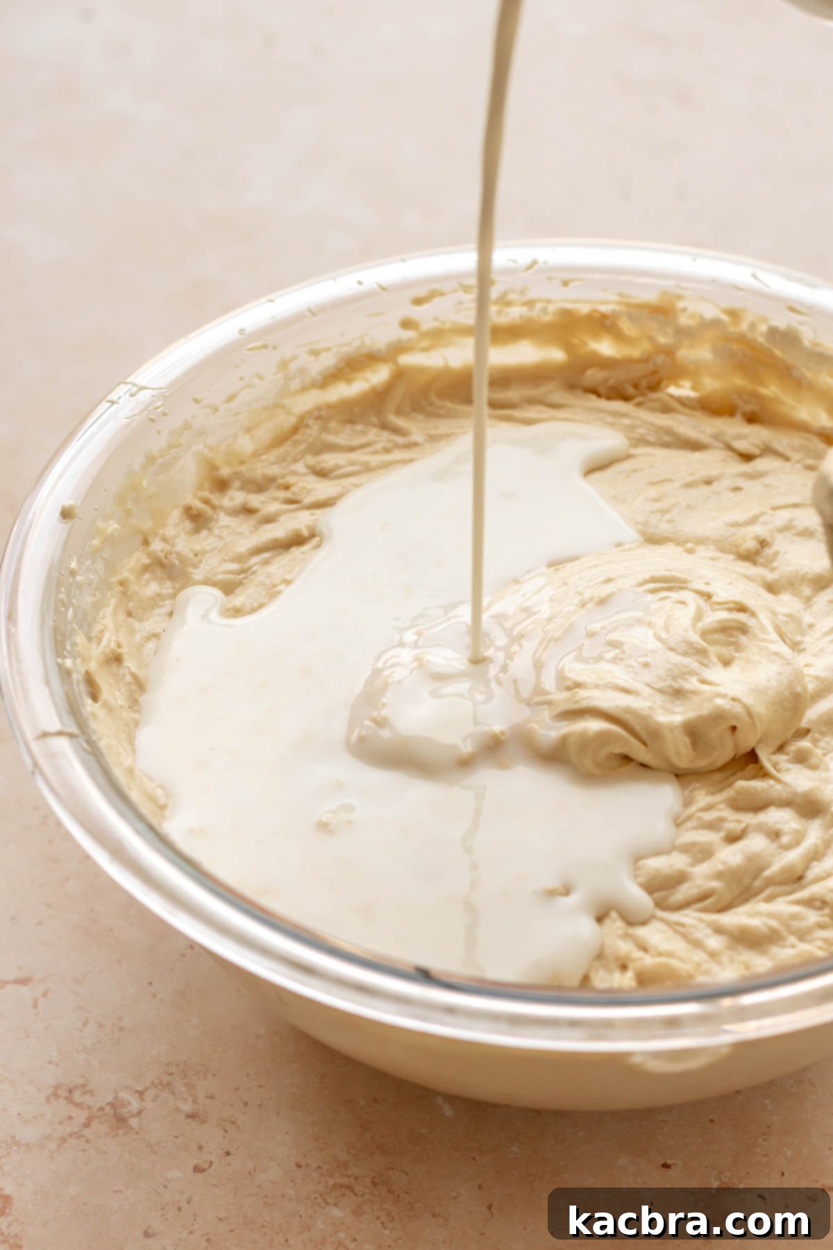 Milk pouring into vanilla cake batter in a bowl.