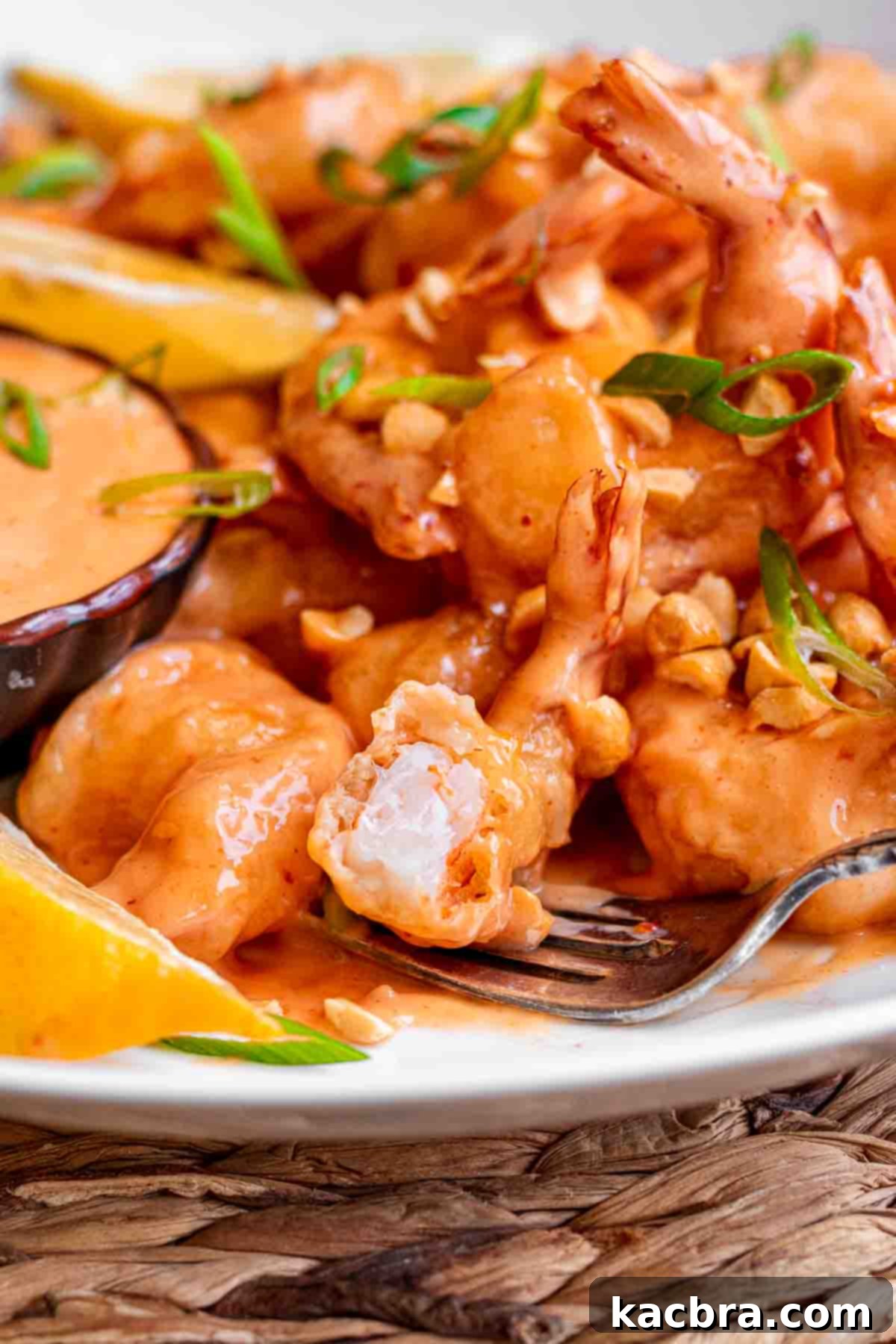 Boom boom shrimp plated on a platter with lemon slices. A fork holds a shrimp with a bite removed.