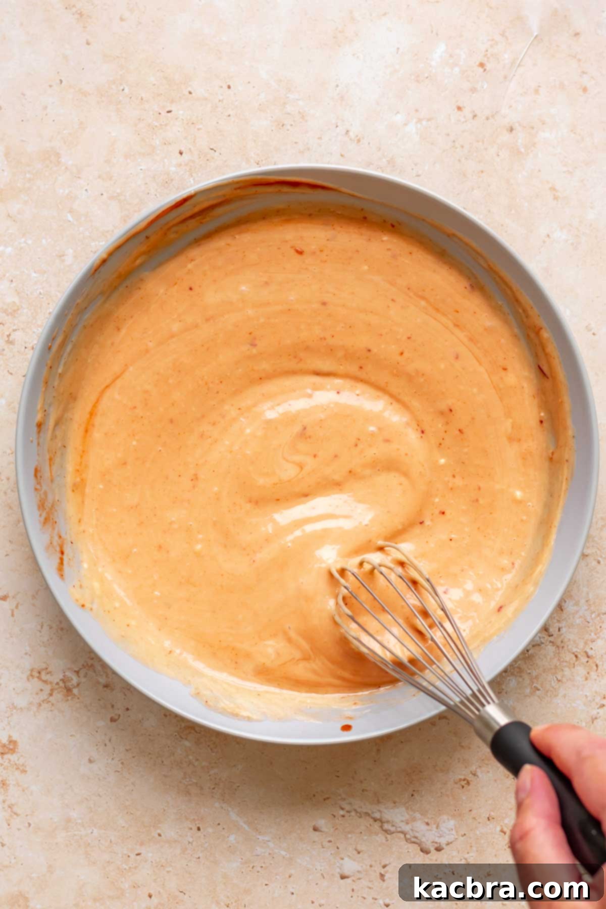 A hand whisks together boom boom sauce in a bowl.