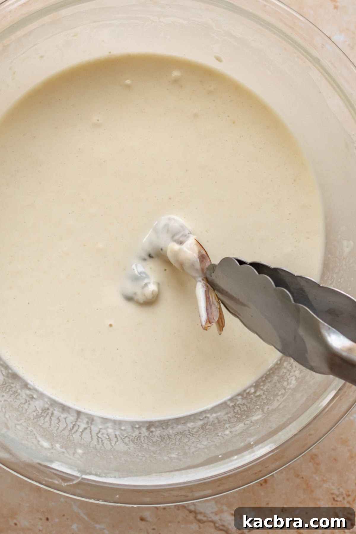 Tongs dip a piece of shrimp into batter.
