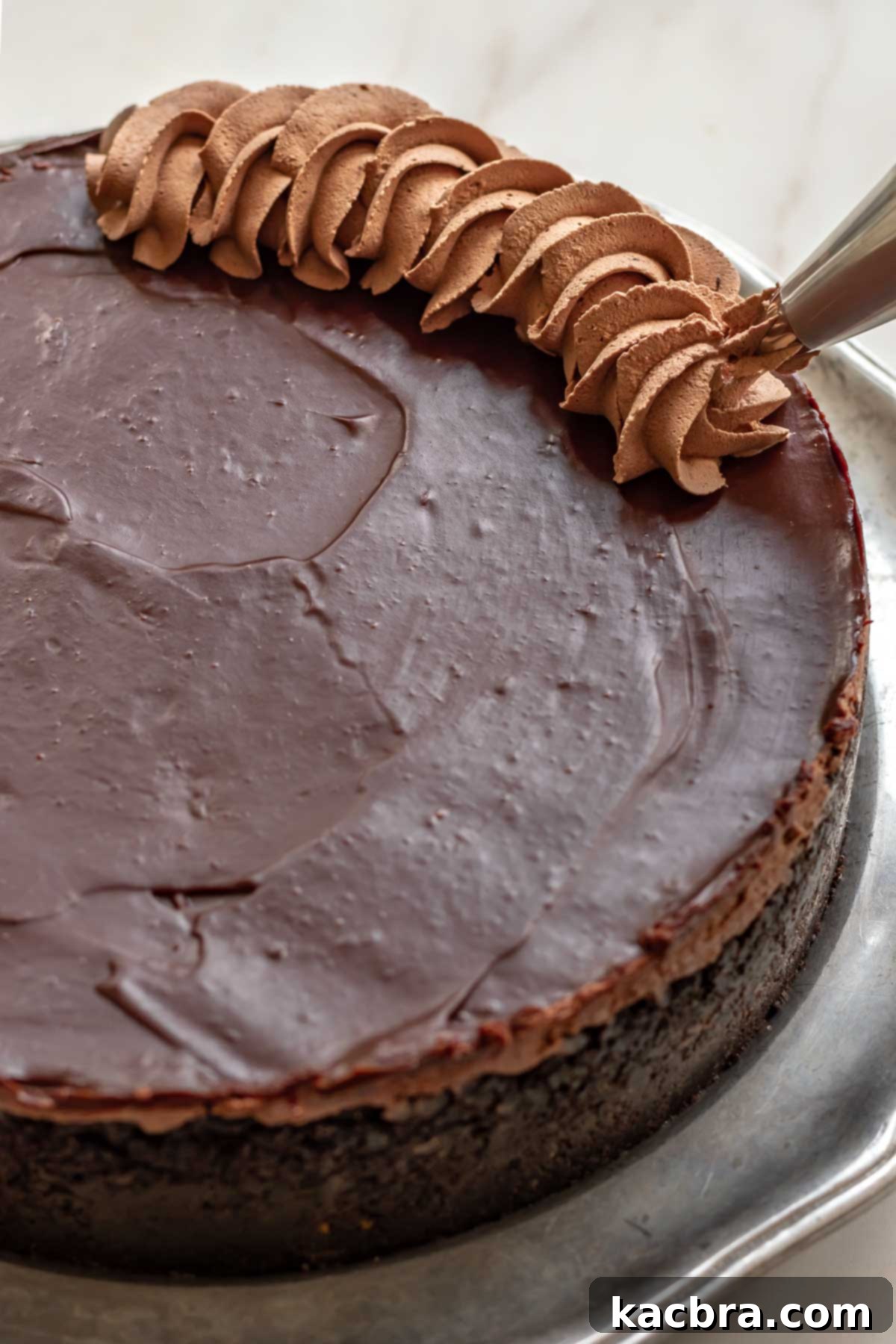 No-Bake Chocolate Orange Velvet Cheesecake 15 A piping bag pipes chocolate whipped cream in a border on the cheesecake.