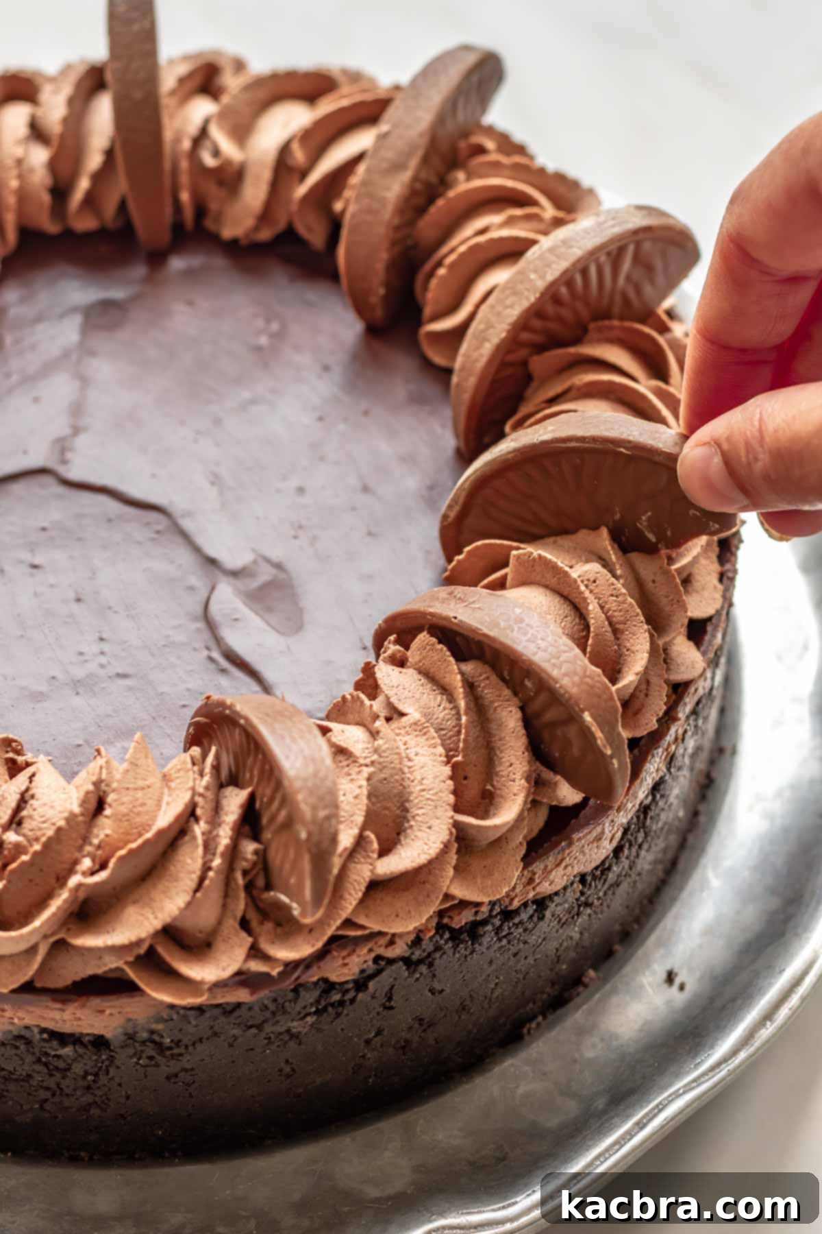 No-Bake Chocolate Orange Velvet Cheesecake 16 A hand adds a piece of chocolate orange into the chocolate whipped cream.