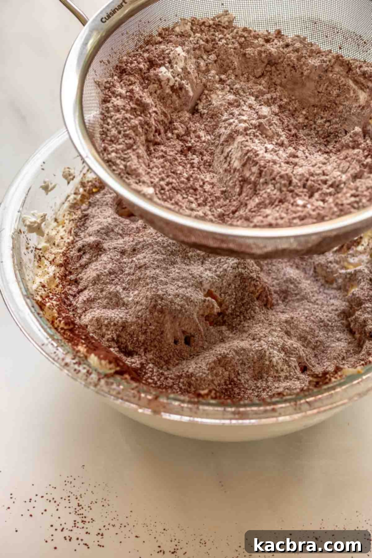 No-Bake Chocolate Orange Velvet Cheesecake 9 Cocoa powder and sugar being sifted into a bowl of cream cheese.