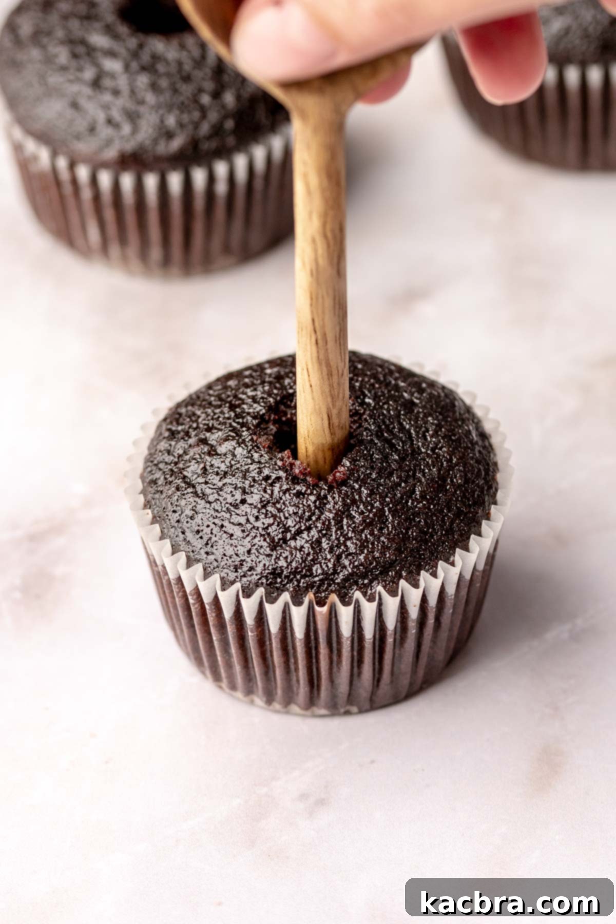 A wooden utensil pushes a hole into the center of a cupcake to make a well.