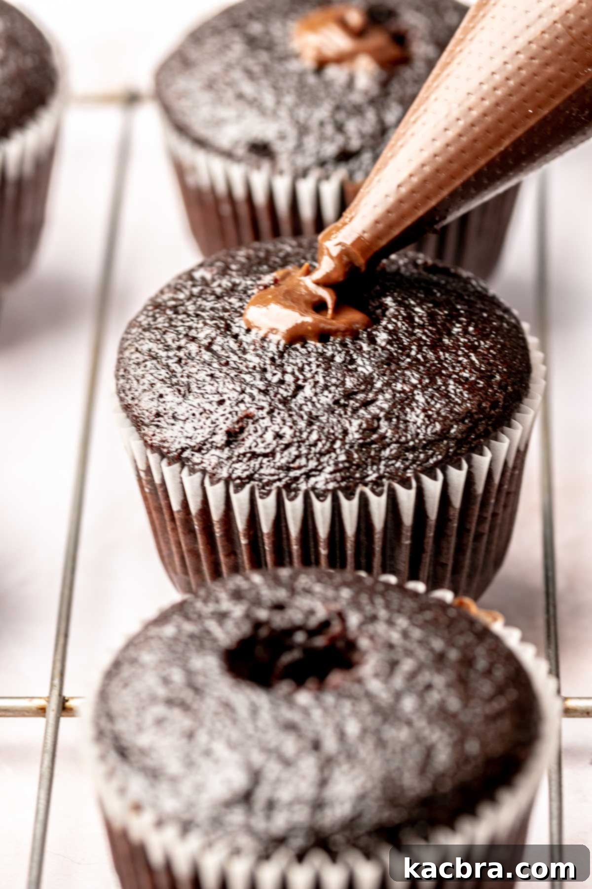 A piping bag adds chocolate ganache into a chocolate cupcake.