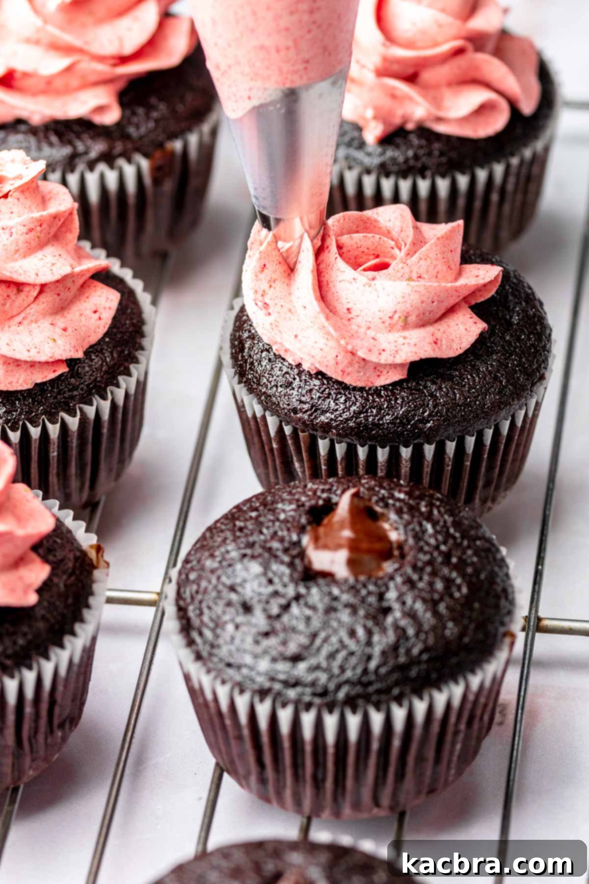 A piping bag adds a swirl of strawberry buttercream onto a cupcake.