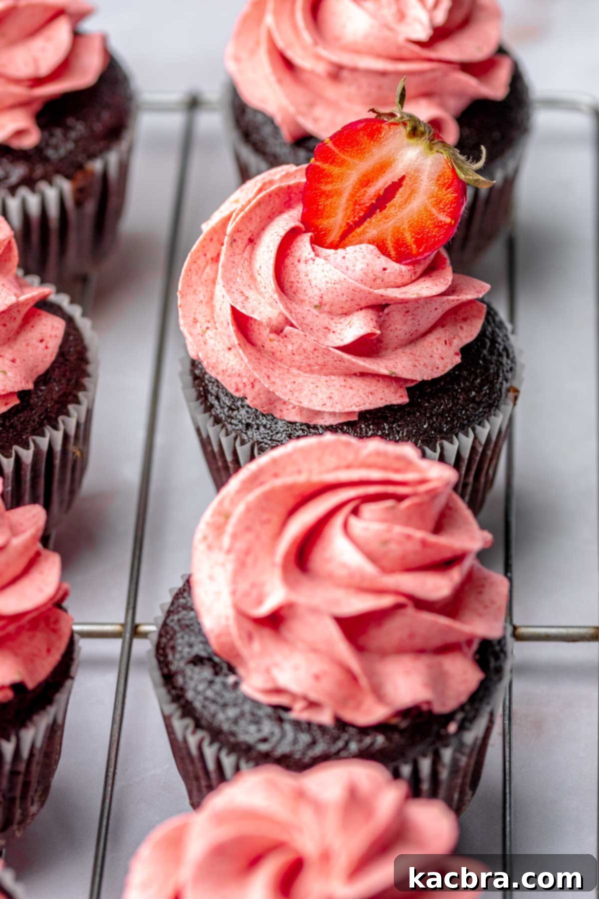 A line of frosted chocolate cupcakes on a wire rack.