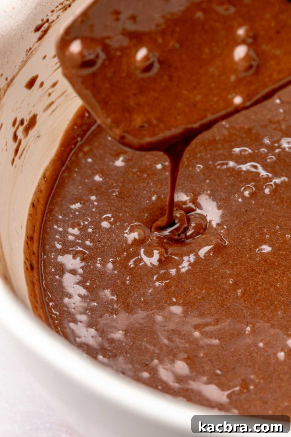Chocolate cupcake batter drips off of a spatula.