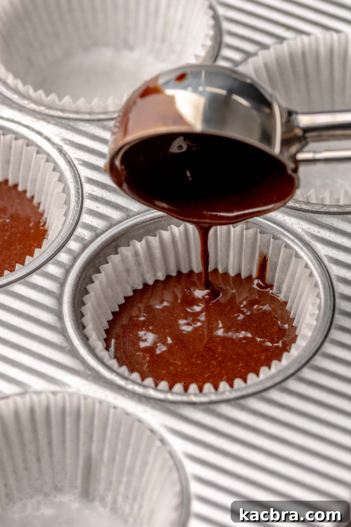 A cookie scoop adds chocolate batter into a muffin tin.