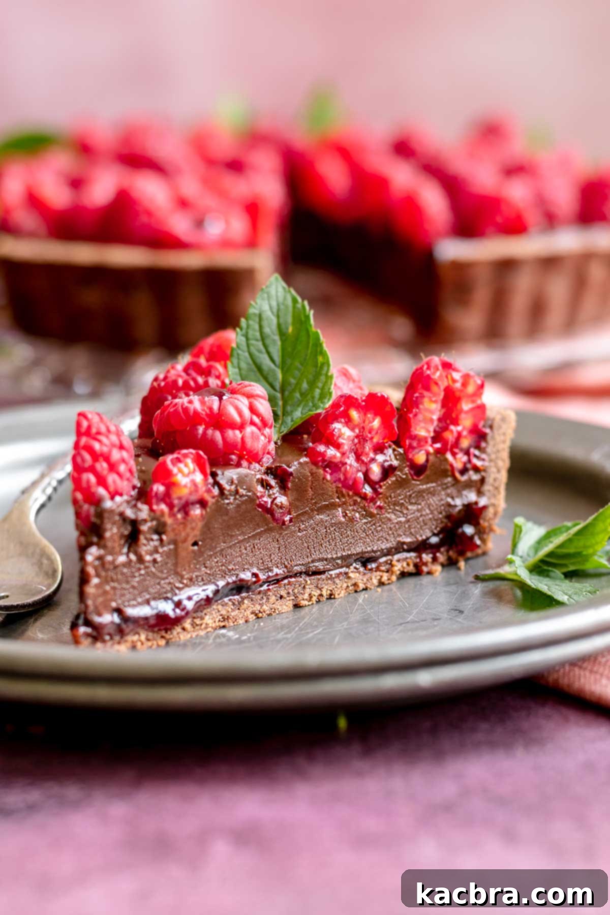 Decadent Chocolate Raspberry Delight 2 A slice of chocolate raspberry tart on a plate, garnished with mint.