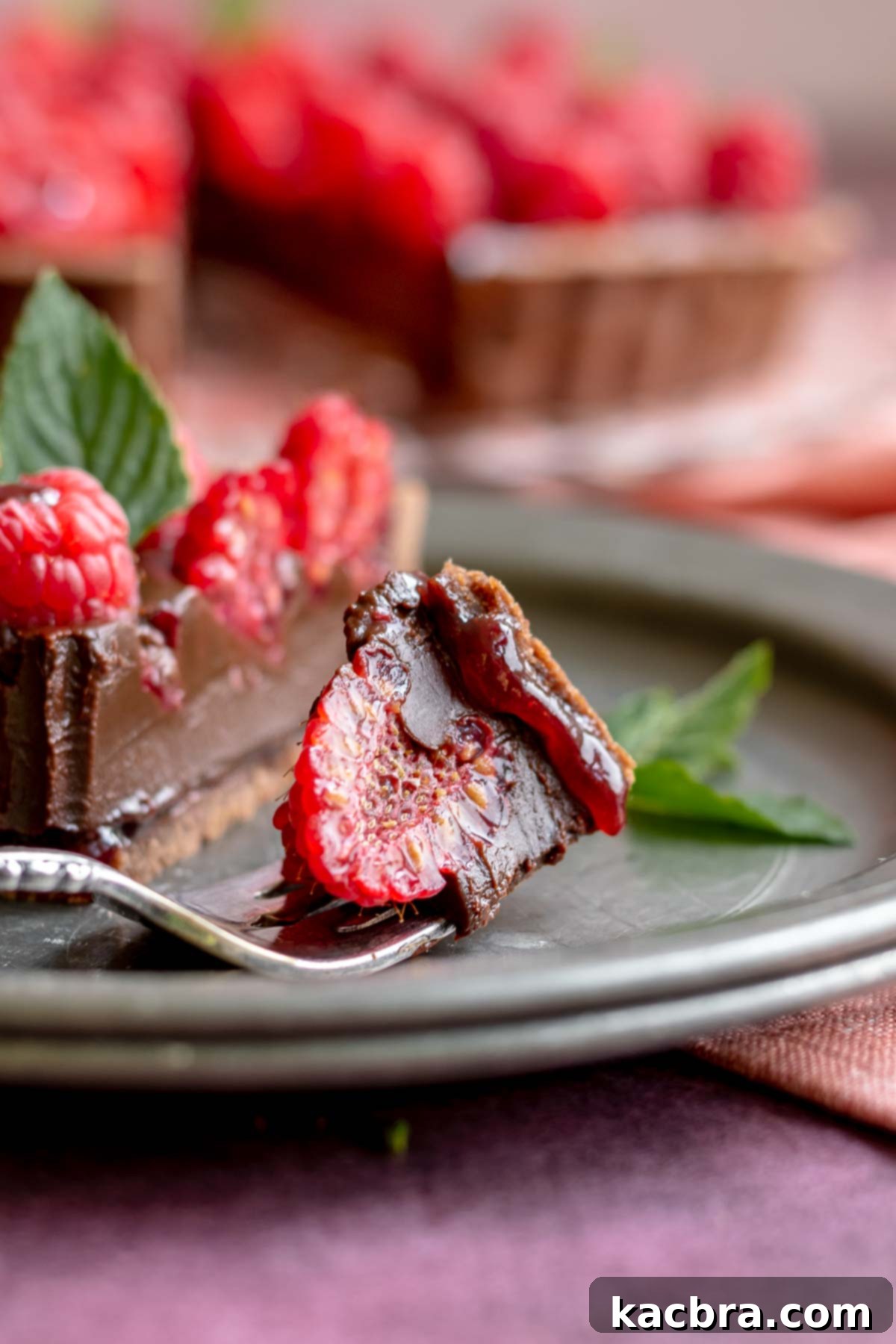 Decadent Chocolate Raspberry Delight 11 A piece of chocolate tart sits on a fork with a raspberry piece in it.