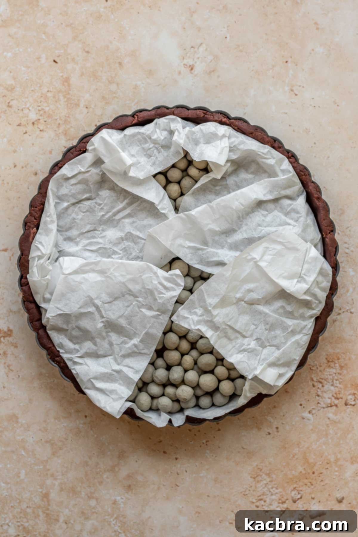 Parchment paper and ceramic pie weights blind baking a chocolate pie tart crust.